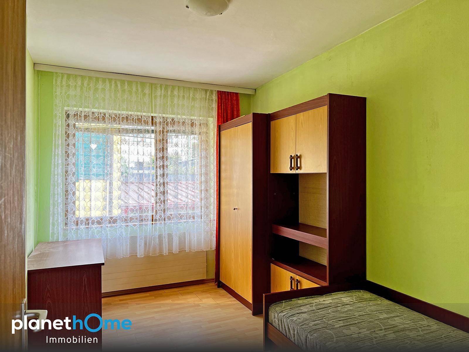Kinderzimmer mit Einzelbett, Schrank und grün gestrichenen Wänden, hell durch das Fenster.