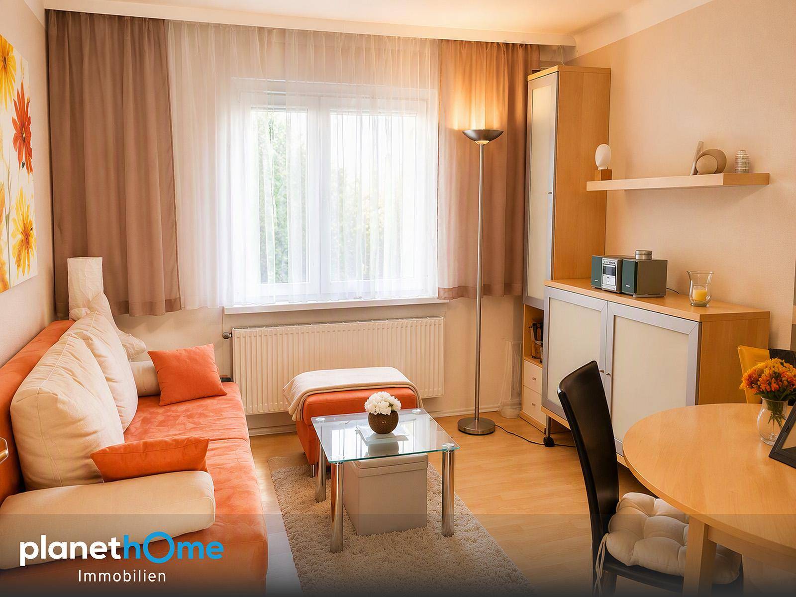 Gemütliches Wohnzimmer mit Sofa, Esstisch, Laminatboden und viel Tageslicht durch das Fenster.