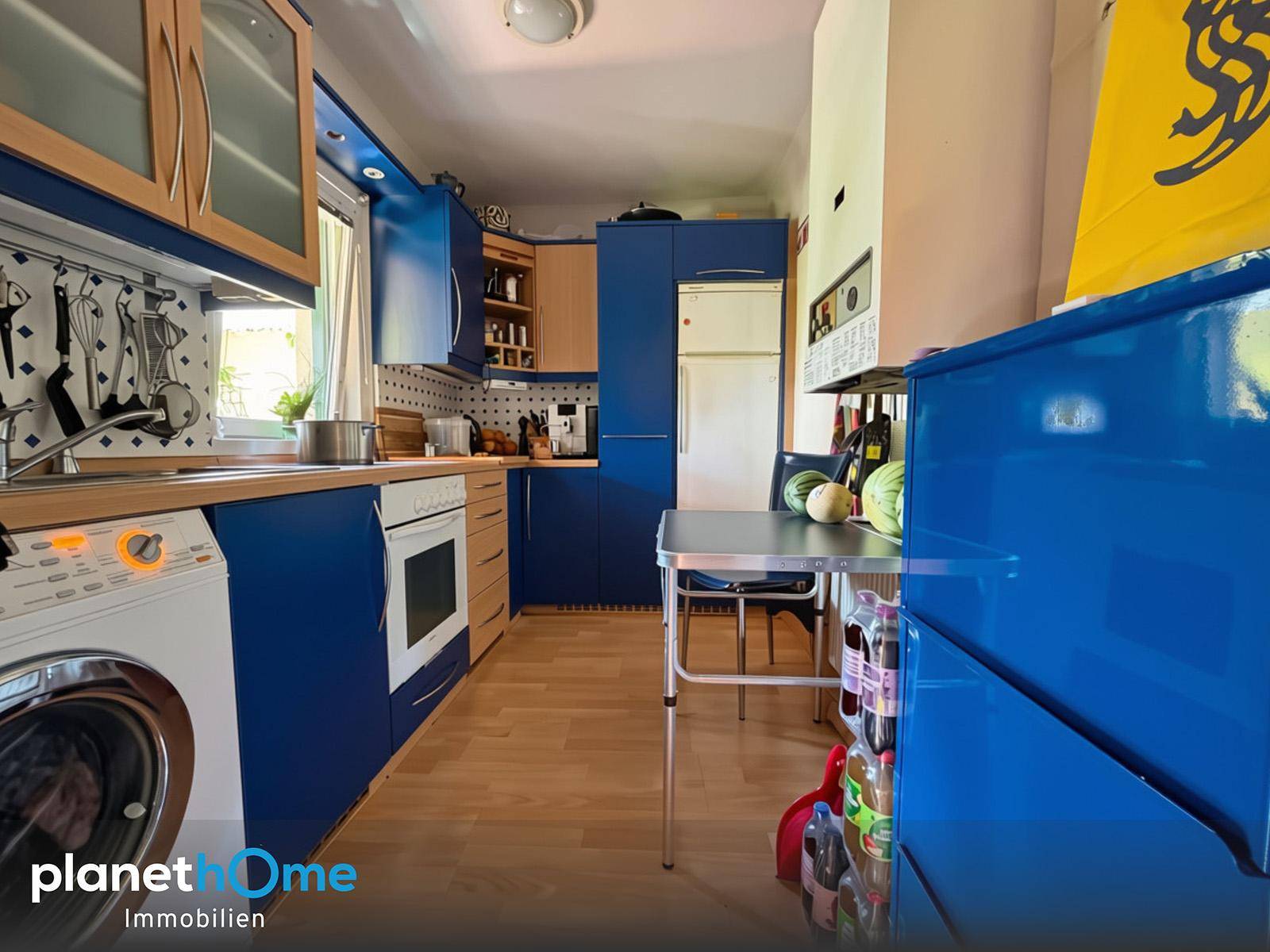 Funktionale Küche mit blauen Schränken, Holz-Arbeitsplatten und integrierten Haushaltsgeräten.