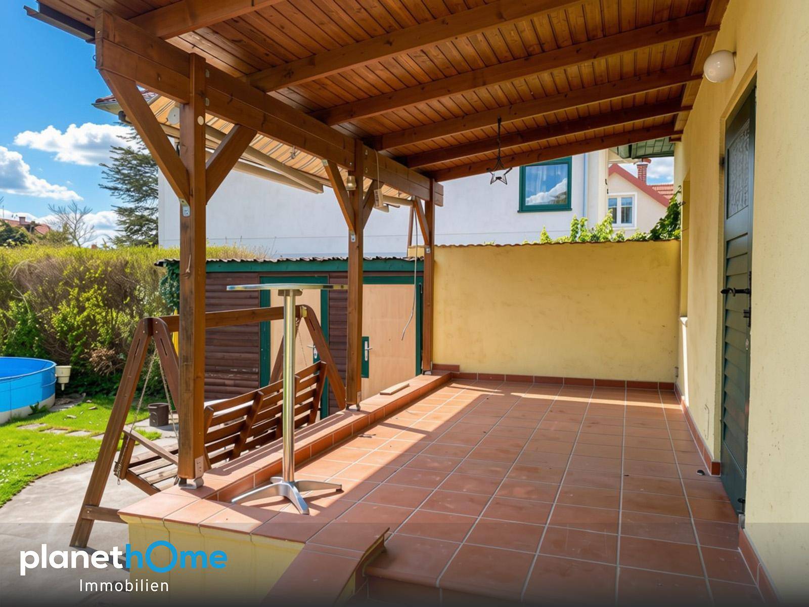 Geräumige überdachte Terrasse mit Schaukel und Blick auf den grünen Gartenbereich.