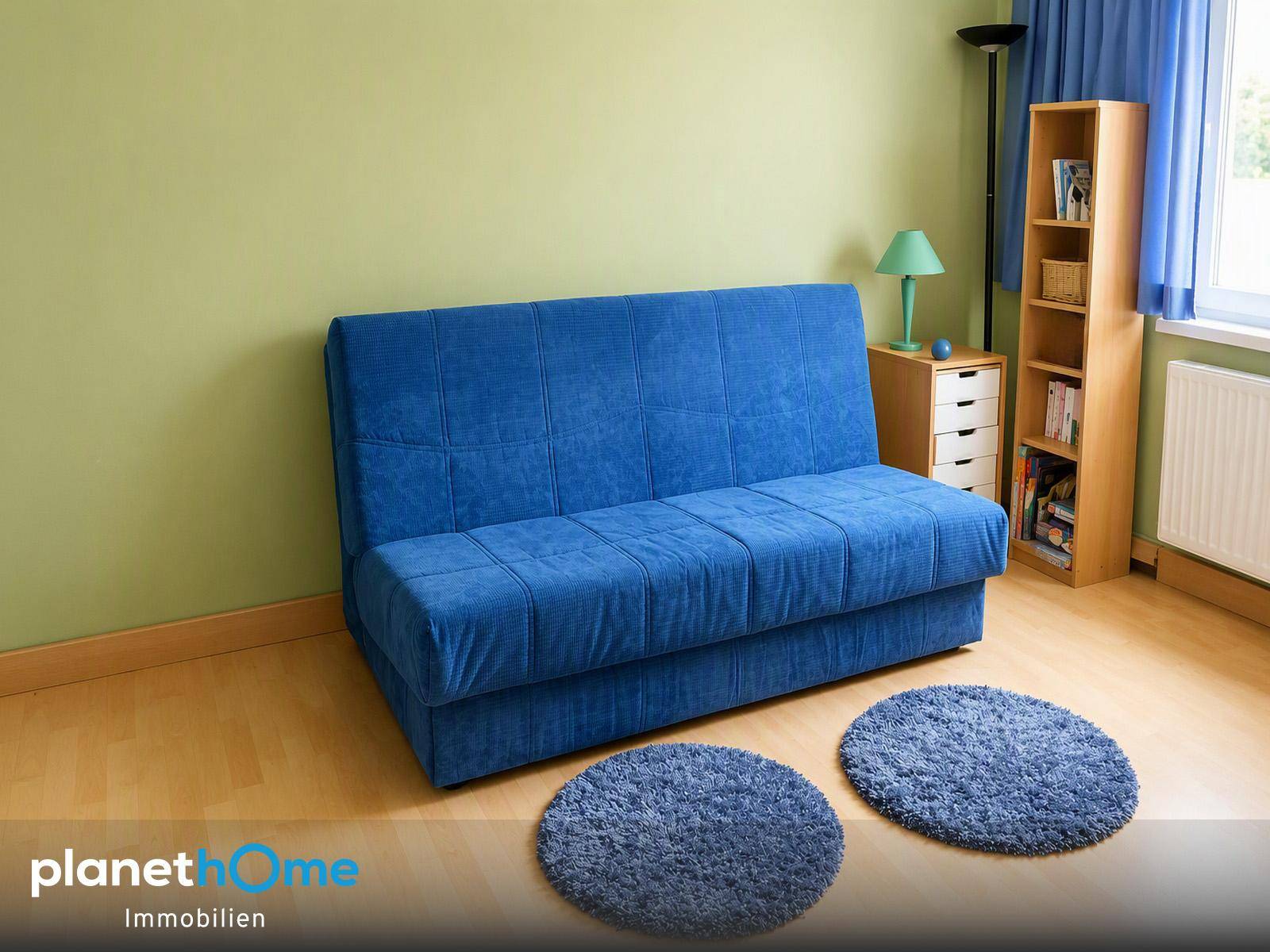 Helles Zimmer mit blauem Schlafsofa, grün gestrichener Wand und Laminatboden.