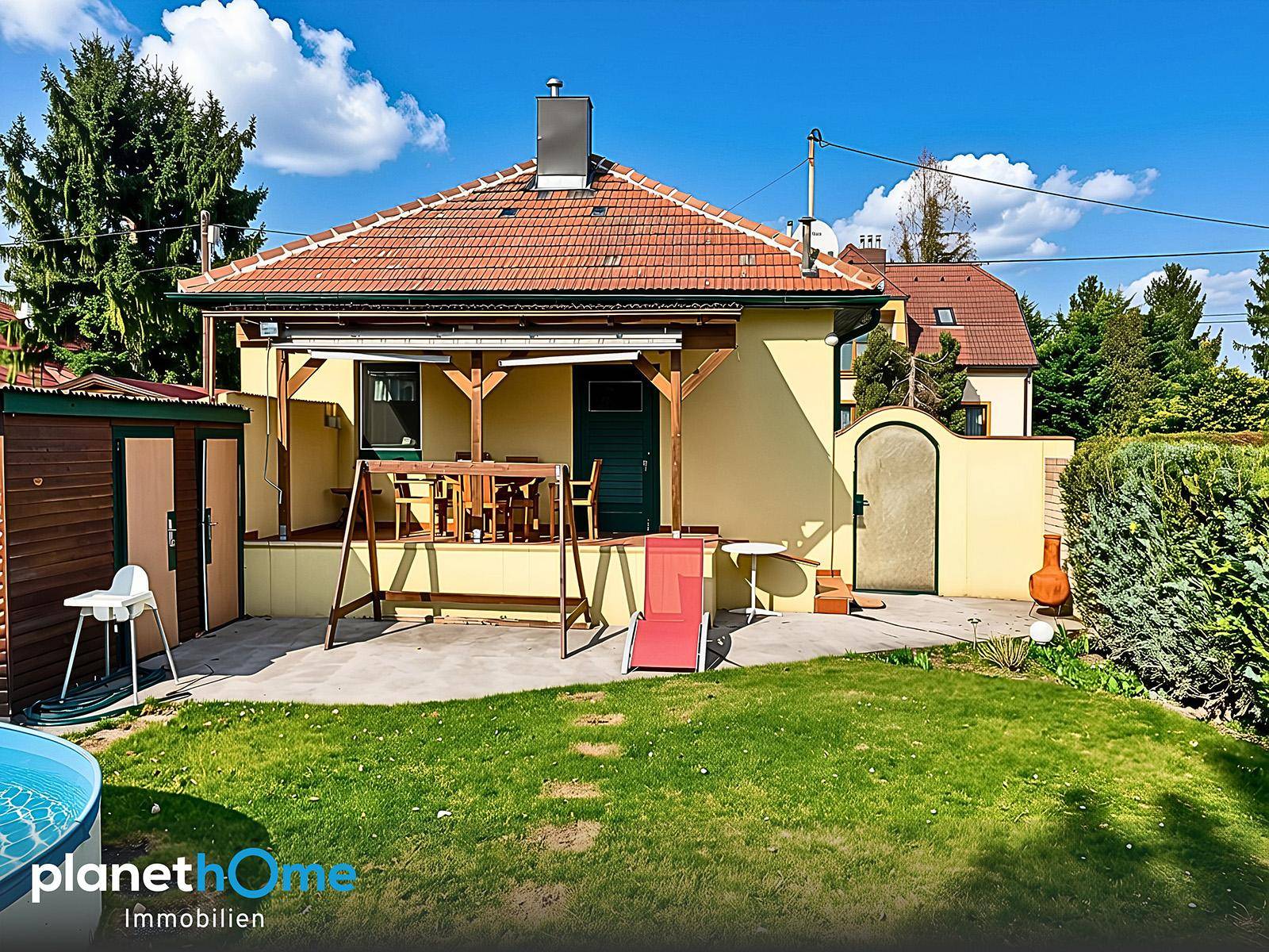 Rückansicht des Hauses mit Terrasse, Gartenmöbeln und weitläufigem Rasenbereich.