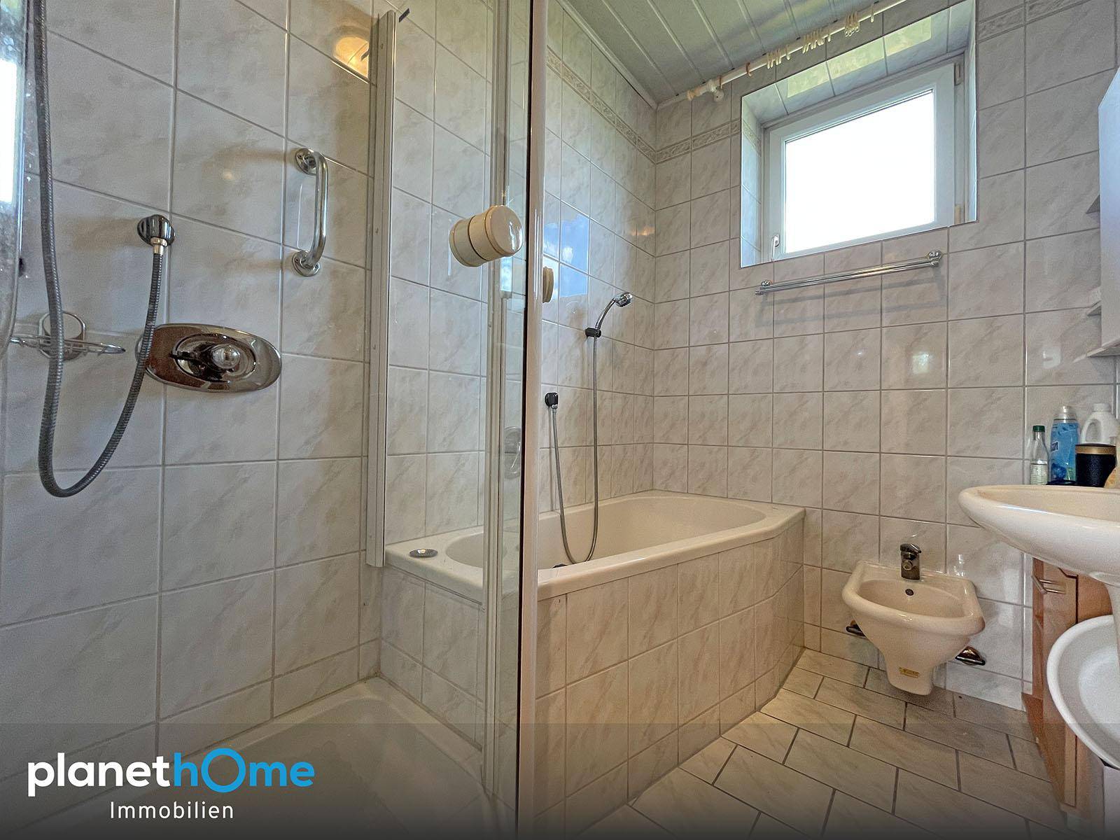 Gefliestes Badezimmer mit Dusche, Eckbadewanne, Bidet und Fenster.