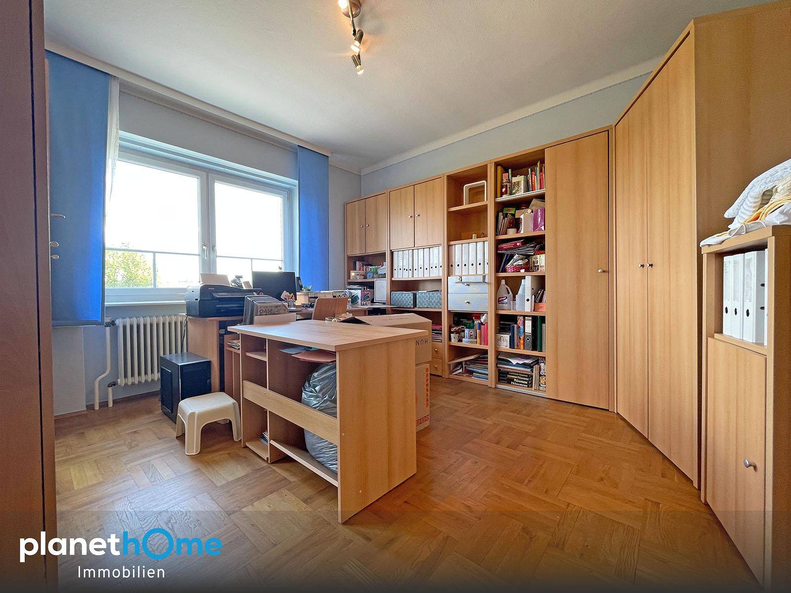 Geräumiges Arbeitszimmer mit Holzparkett, großen Fenstern und viel Stauraum.