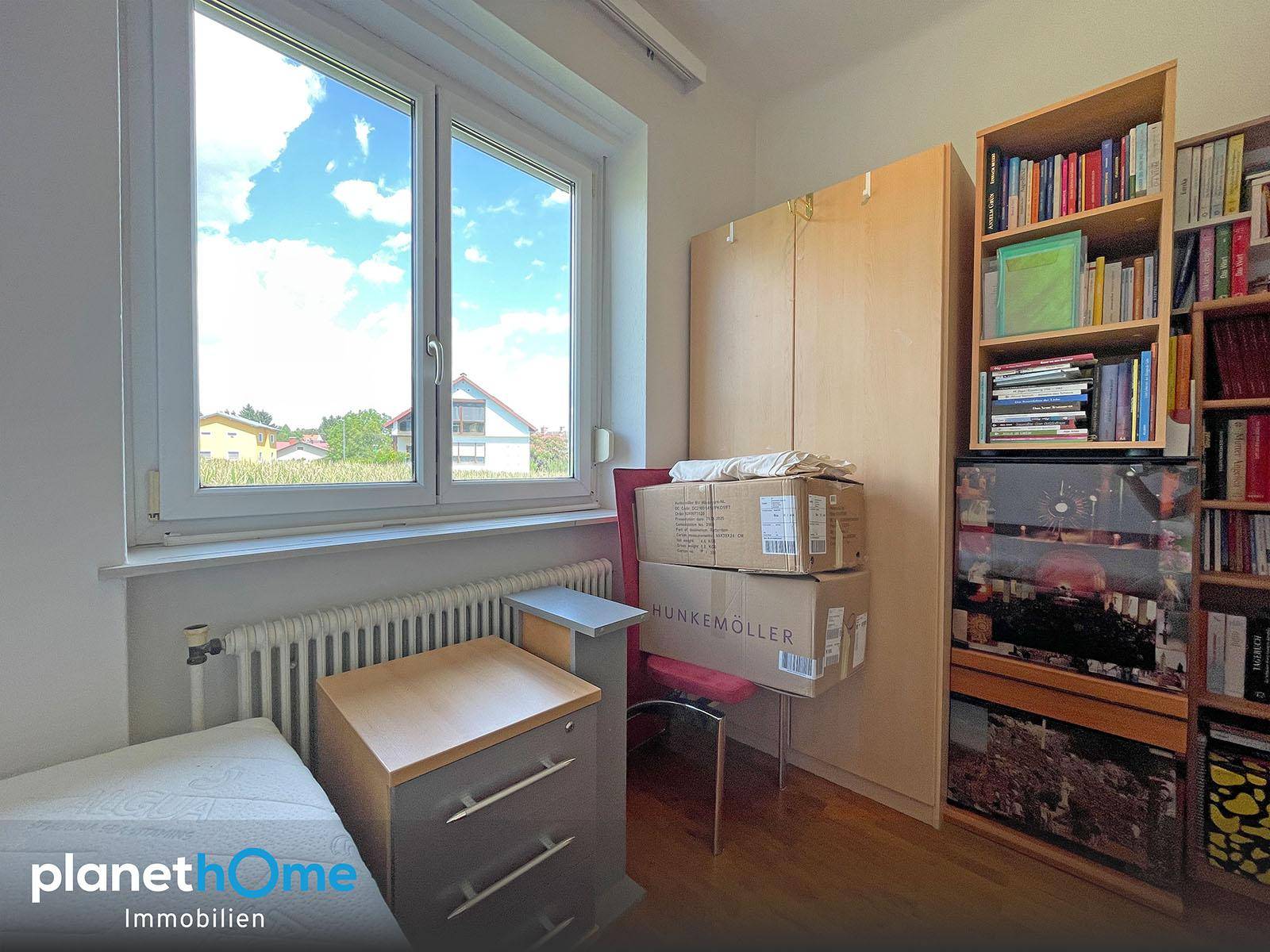 Helles Schlafzimmer mit Fensterblick ins Grüne und praktischen Holzregalen.