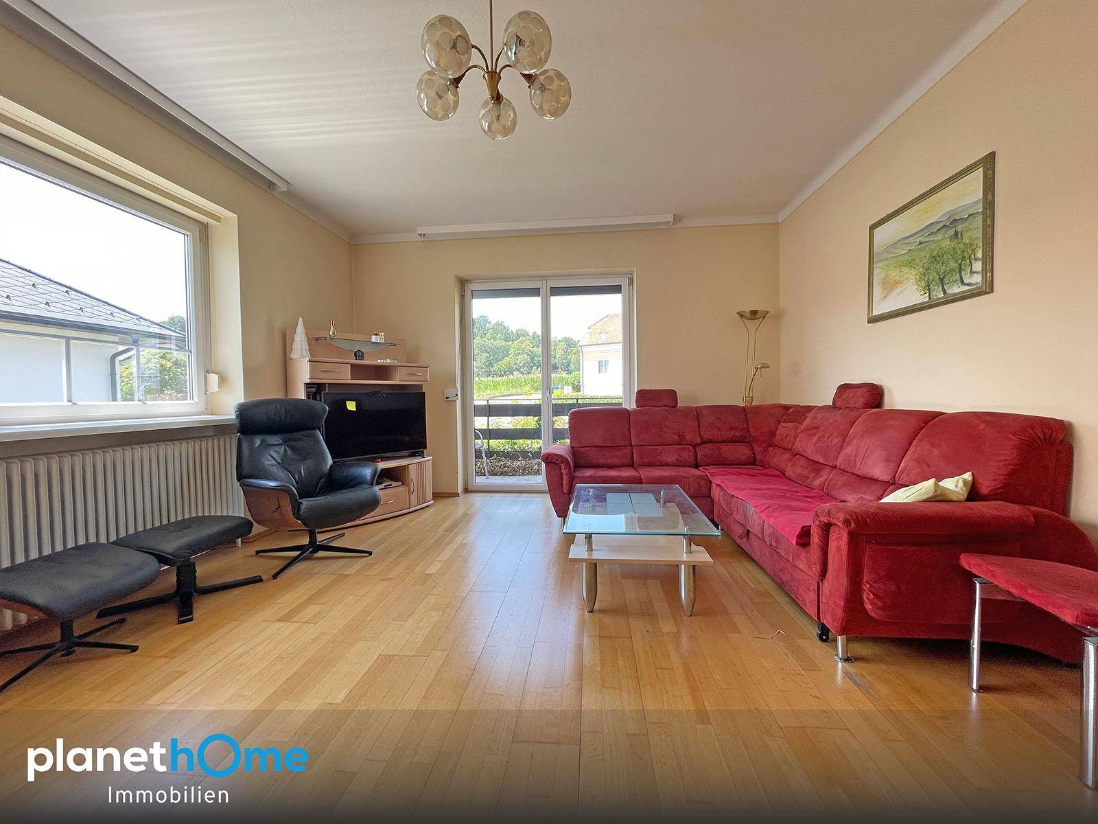 Geräumiges Wohnzimmer mit rotem Ecksofa, Parkettboden und Zugang zum Balkon.