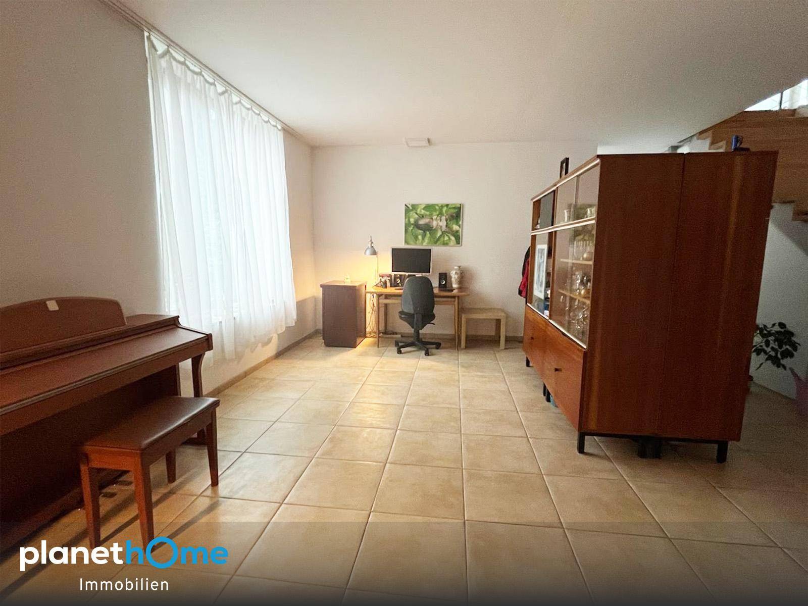 Geräumiger Arbeitsbereich mit Fliesenboden, Schreibtisch und einem Klavier, ideal für Home-Office.