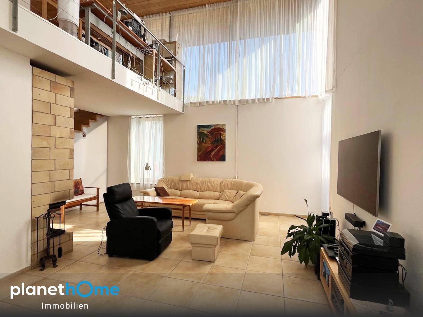 Helles Wohnzimmer mit hohen Decken, Fliesenboden und einer offenen Galerie mit Treppe.
