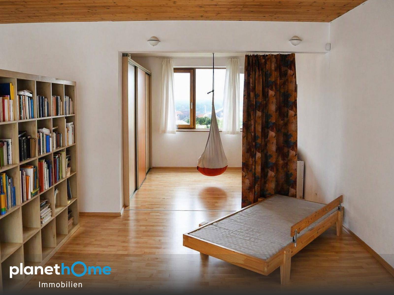 Schlafzimmer mit Holzboden, Bücherregal und Zugang zu einem weiteren hellen Raum.