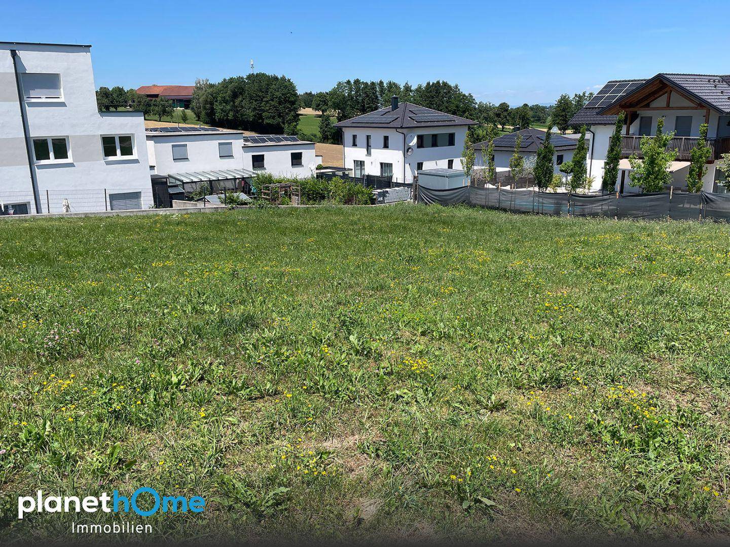 Weitläufiges, sonniges Baugrundstück mit Blick auf moderne Wohnhäuser in ländlicher Umgebung.