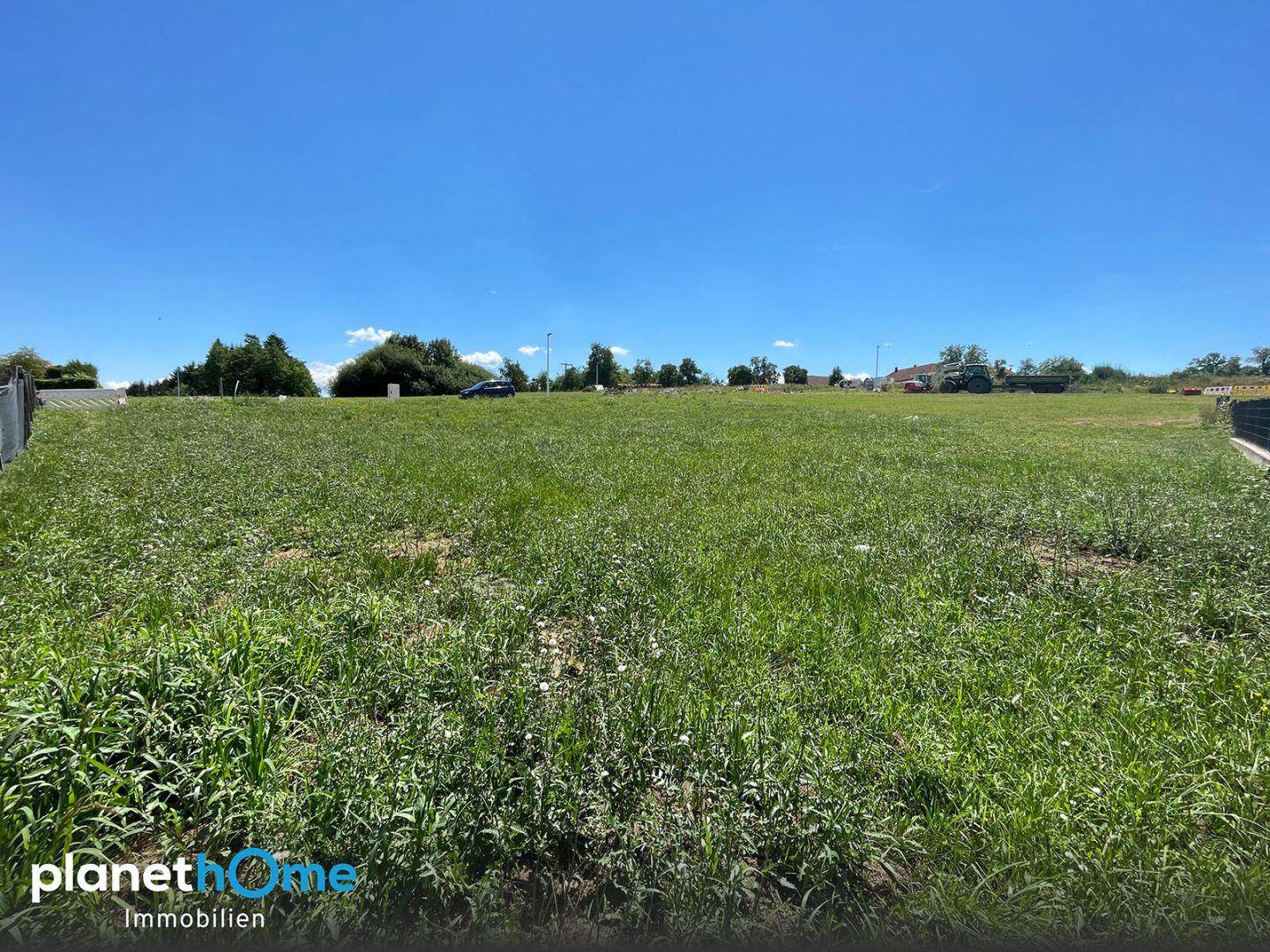 Weitläufiges, unverbautes Baugrundstück unter blauem Himmel mit Fernblick in die Natur.