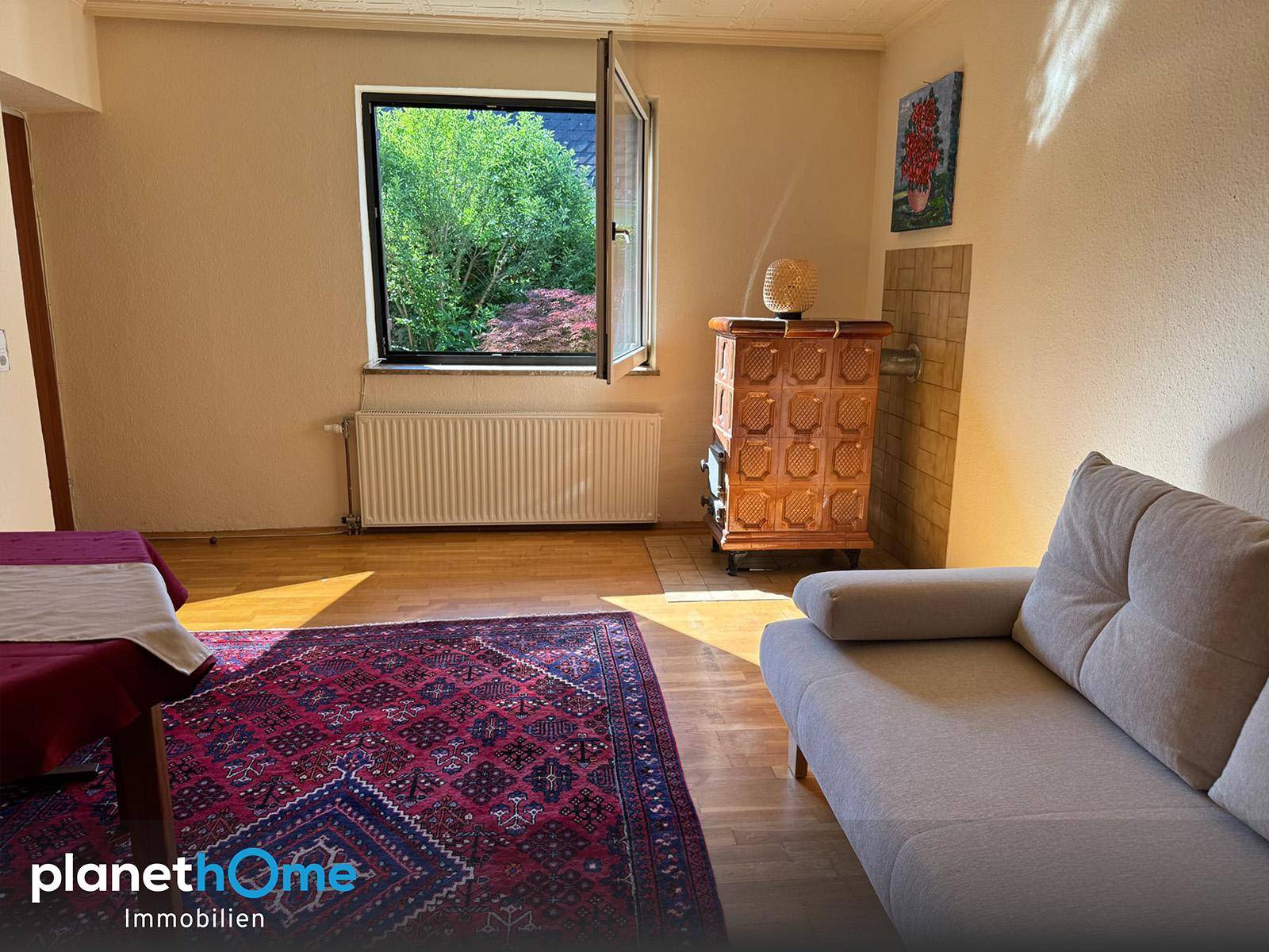 Gemütlicher Wohnbereich mit Holzofen, Sofa und Fenster mit Blick ins Grüne.