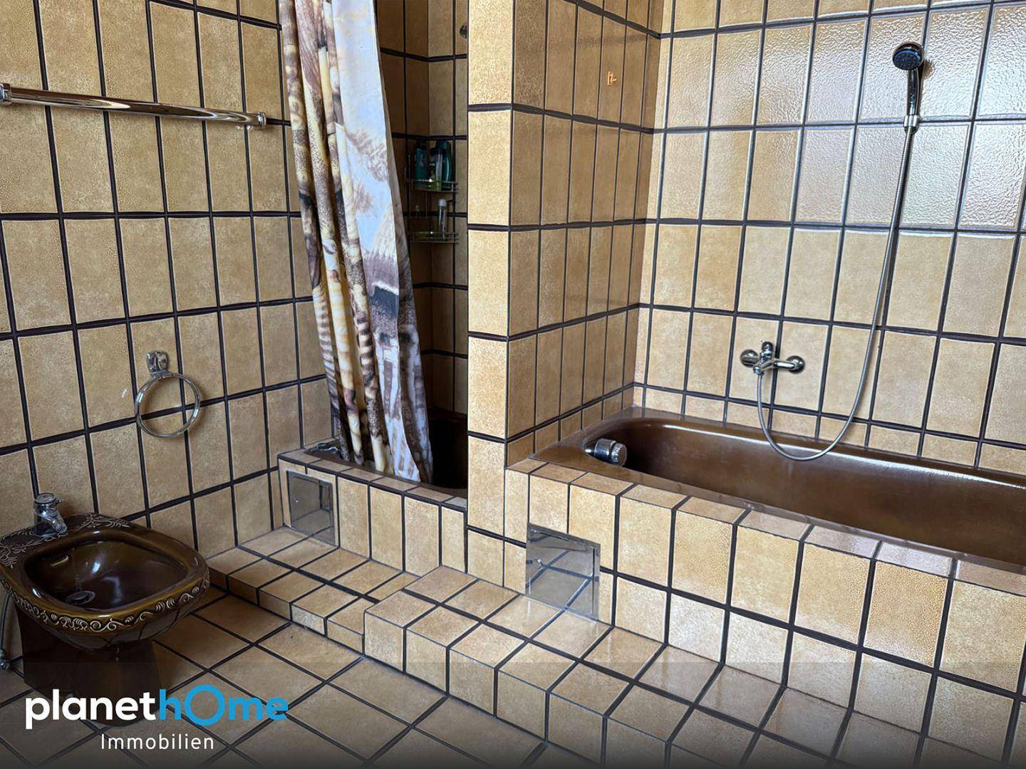 Badezimmer mit braunen Fliesen, Badewanne, Duschbereich und Bidet, im Stil der 80er Jahre.