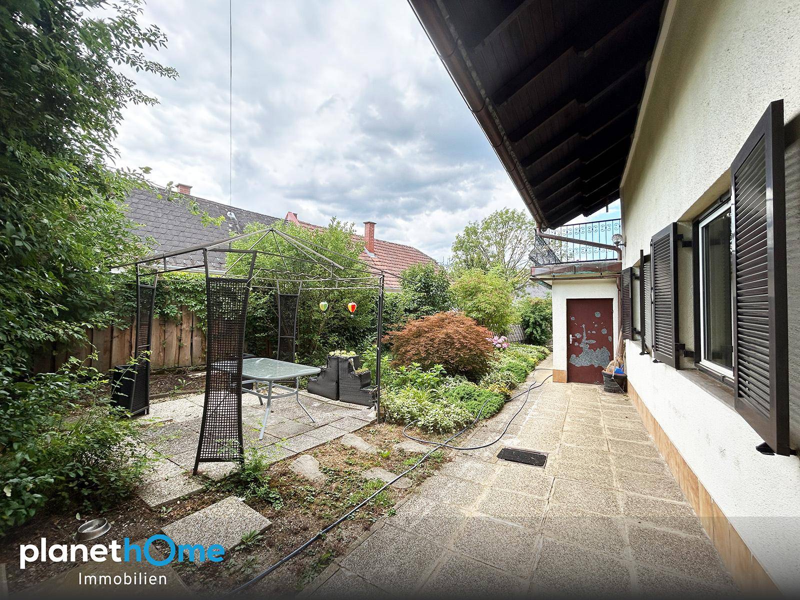 Seitenansicht des Hauses mit gepflastertem Weg, Gartenbereich und einem Pavillon.