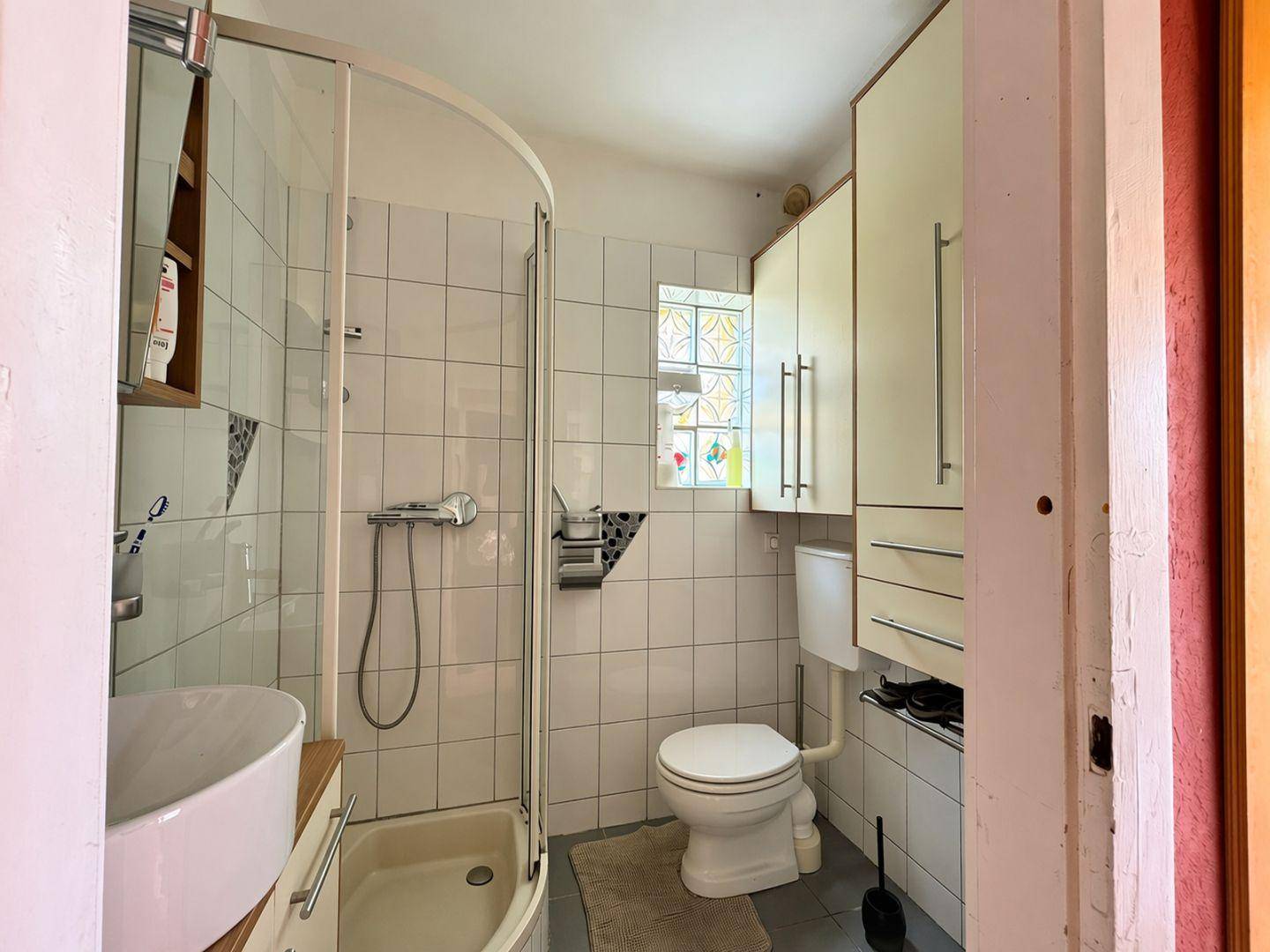 Funktionales Badezimmer mit Duschkabine, Toilette, Waschbecken und einem kleinen Fenster.