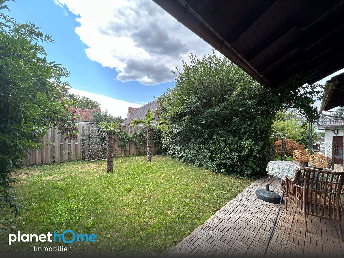 Gepflegter Garten mit Rasenfläche, Palmen und einer Terrasse mit Sitzgelegenheiten.