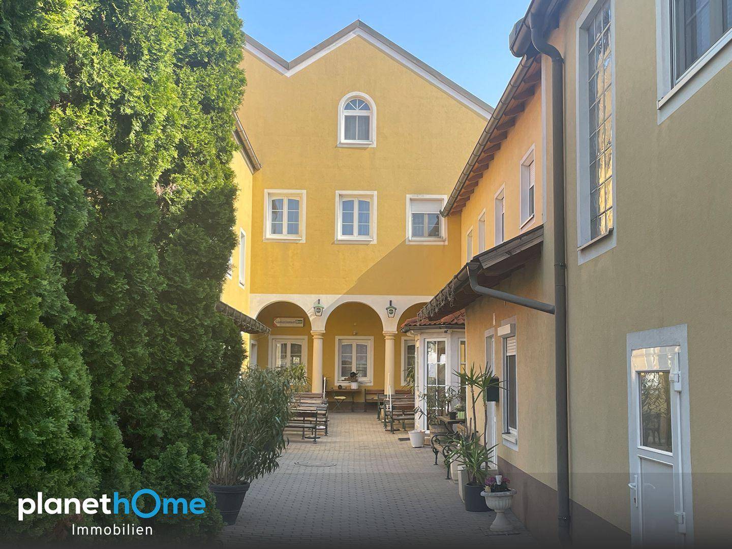 Innenhof mit Arkaden, Sitzgelegenheiten und hohen Bäumen, der zum Verweilen einlädt.