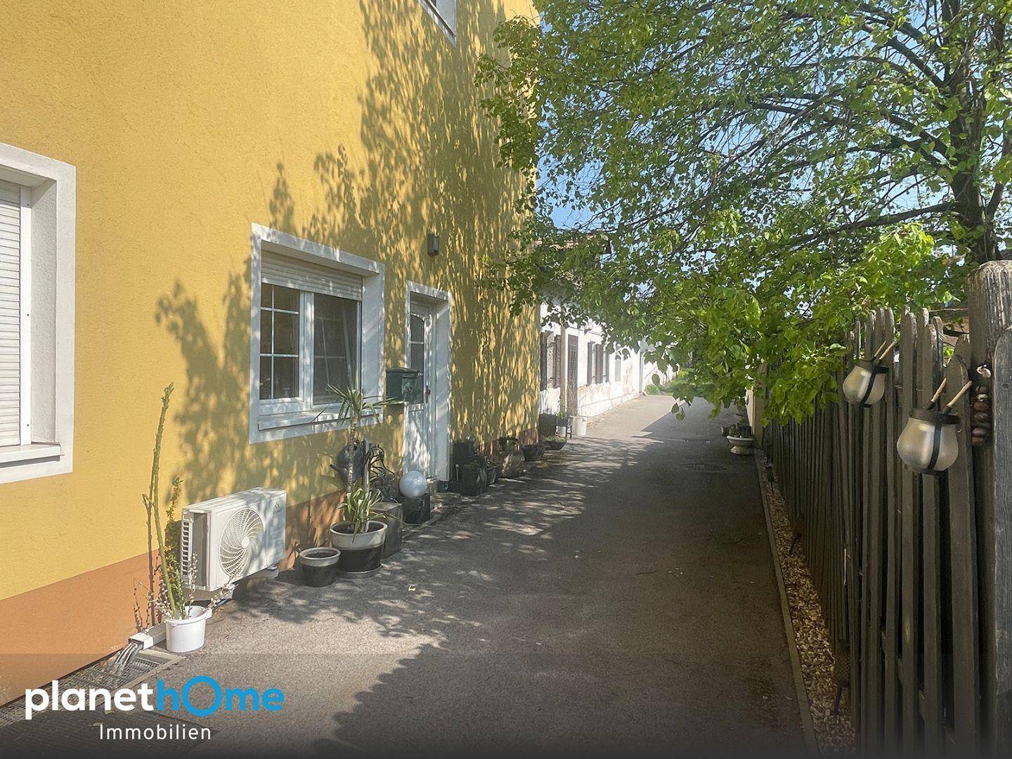 Seitenansicht eines gelben Gebäudes mit einem schmalen Weg und Pflanzen entlang der Wand.