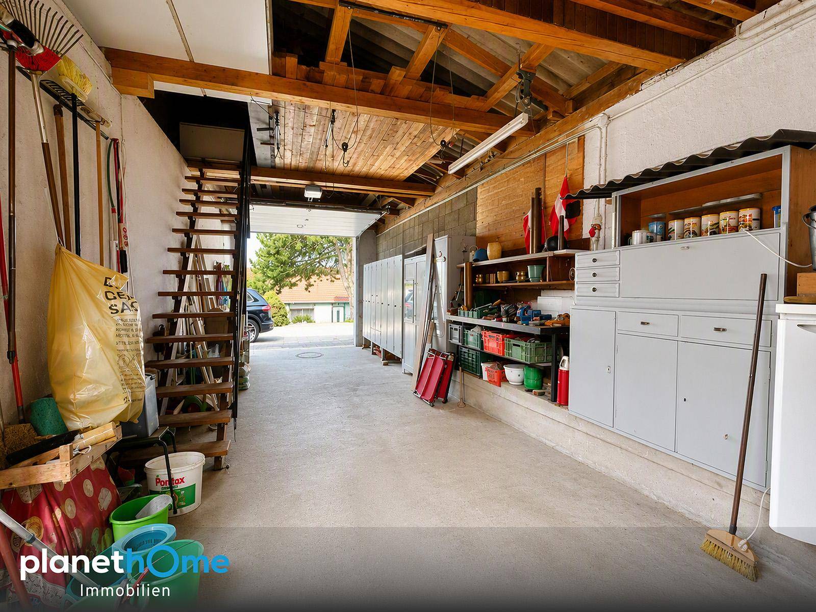 Geräumige Garage oder Werkstatt mit Betonboden, Holzdecke und viel Stauraum für Werkzeuge.