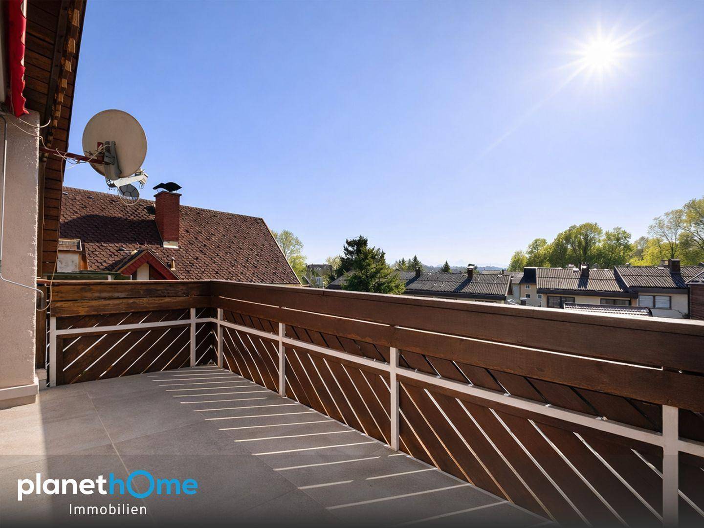 Sonniger Balkon mit Fliesenboden und Holzbalkongeländer, bietet einen weiten Blick über die Dächer.