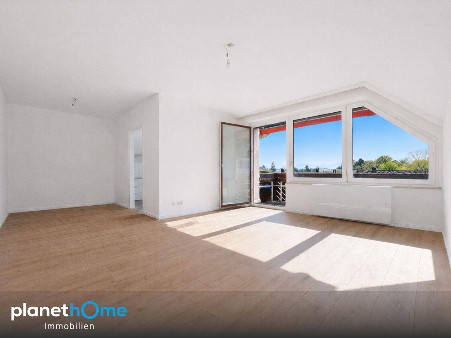 Helles Wohnzimmer mit Holzboden, weißen Wänden und Zugang zu einem Balkon unter Dachschräge.