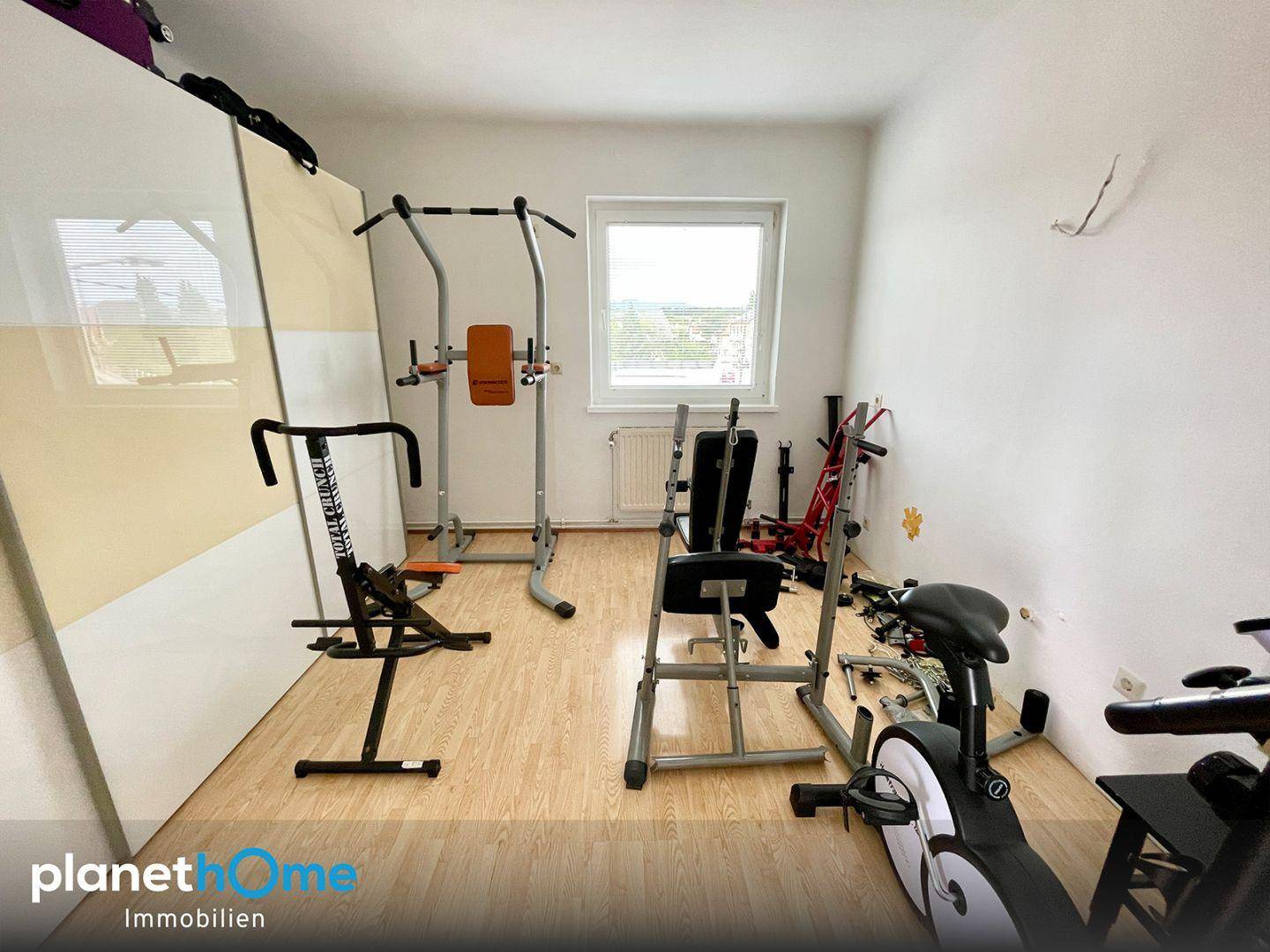 Raum eingerichtet als Fitnessbereich mit verschiedenen Trainingsgeräten und Laminatboden.