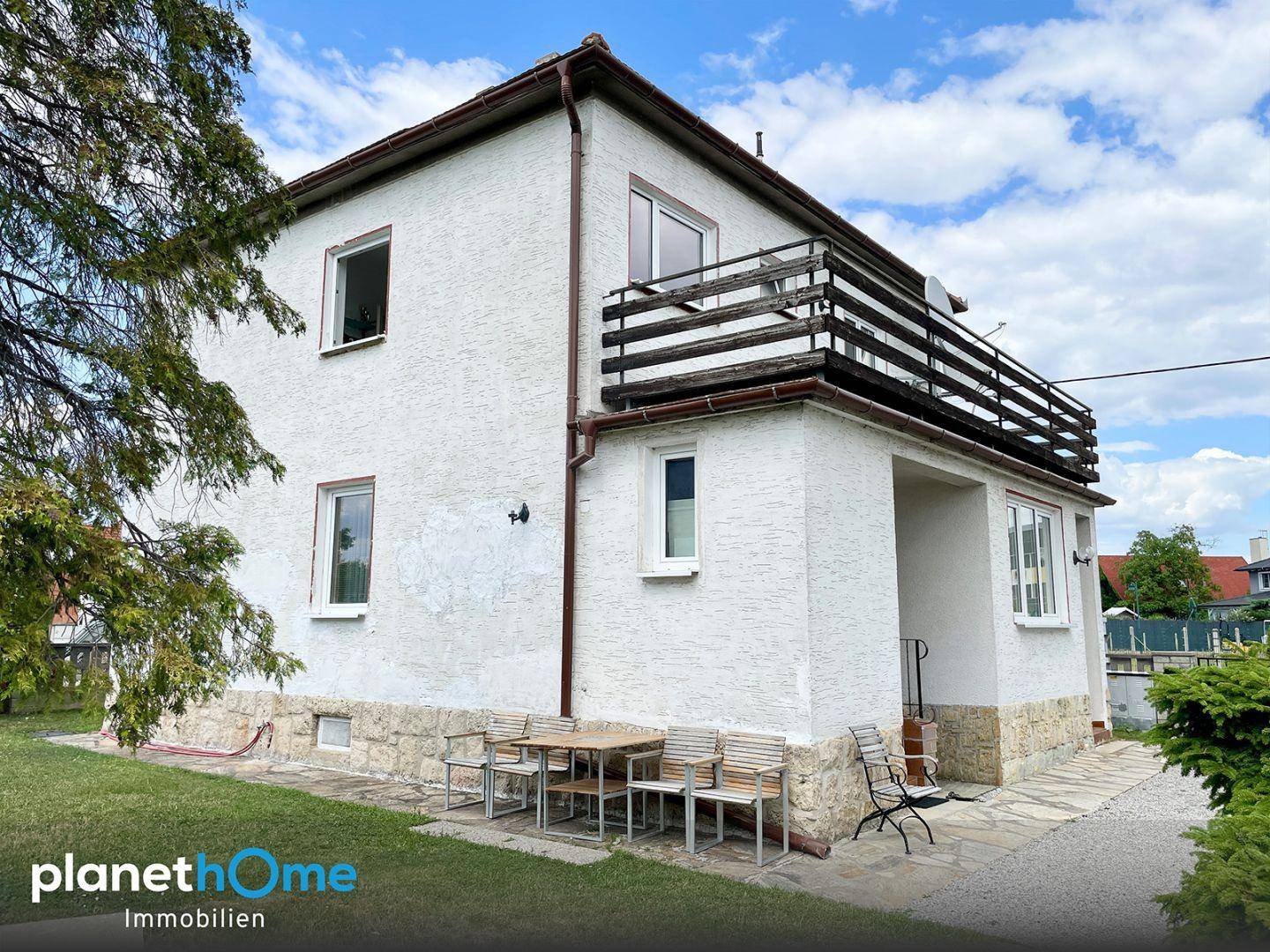 Ansicht des weißen Einfamilienhauses von der Seite mit Terrasse und Balkon im Obergeschoss.