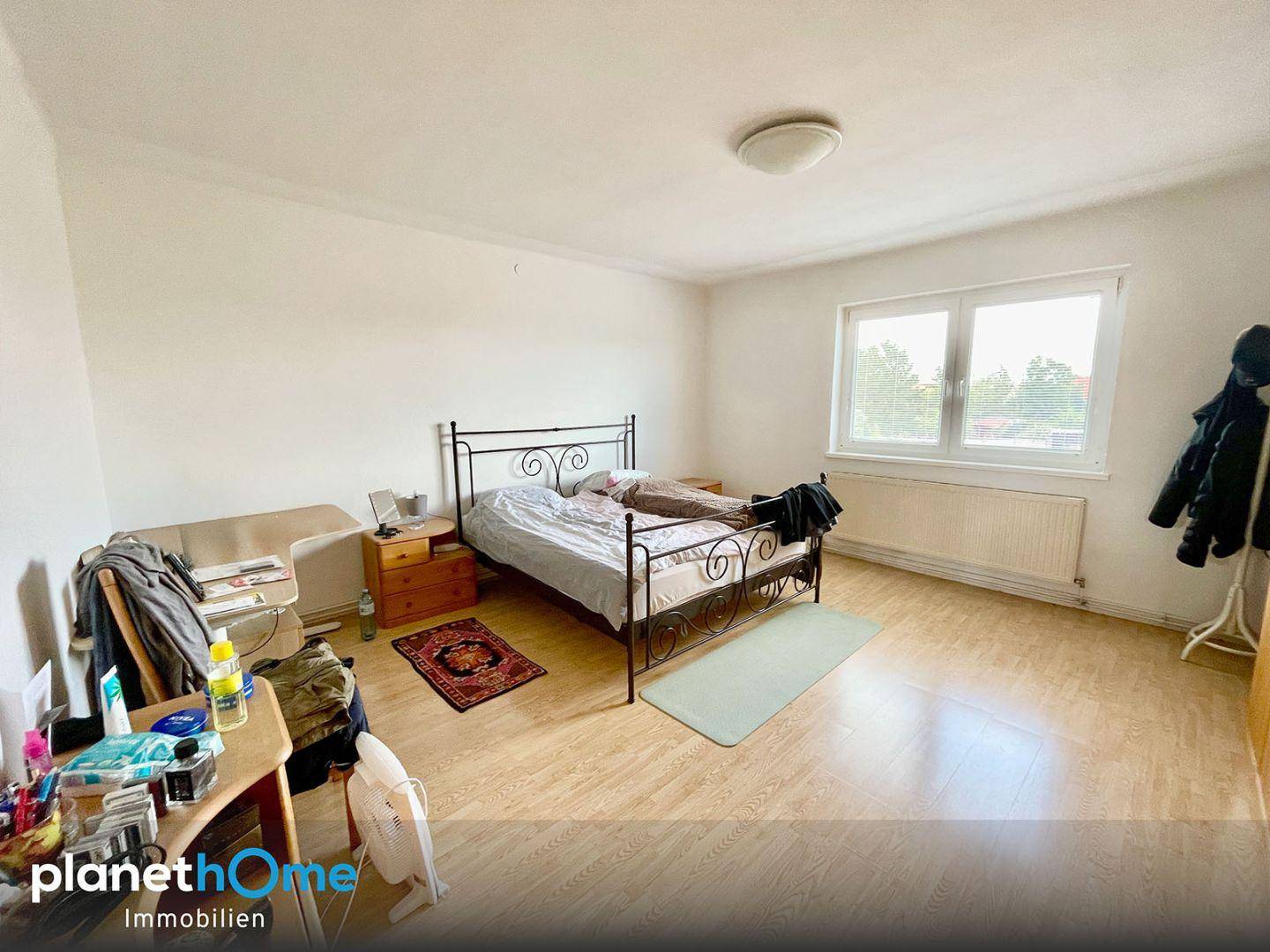 Helles Schlafzimmer mit Laminatboden, Doppelbett und Fenster mit Blick ins Grüne.