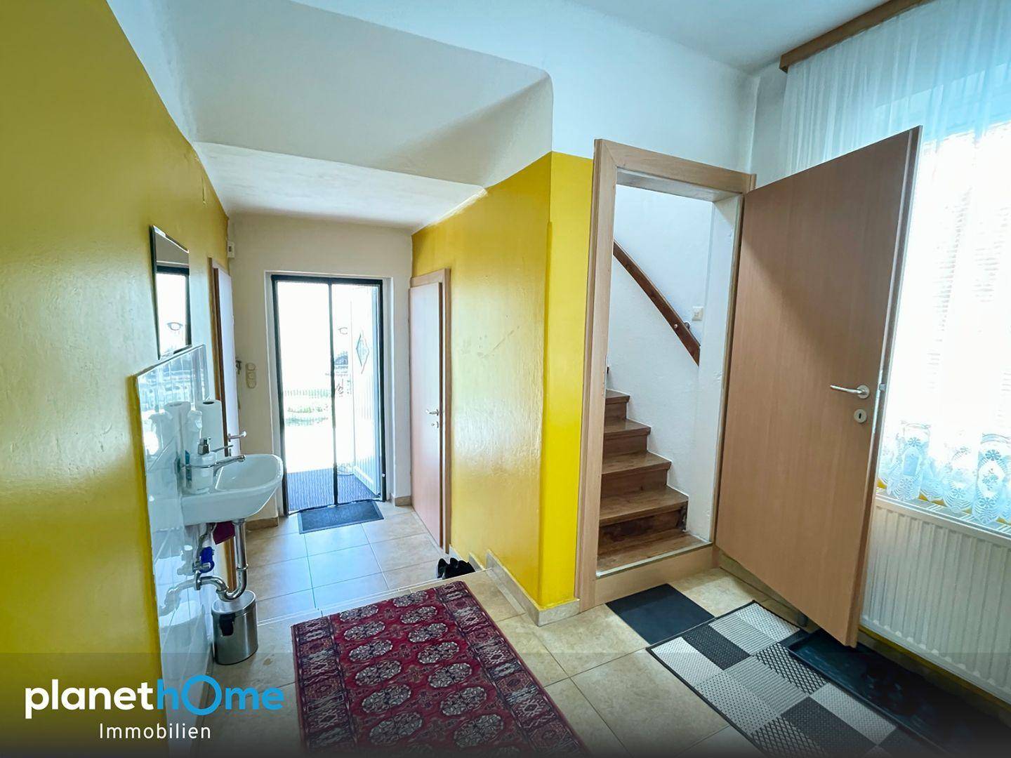 Heller Eingangsbereich mit gelben Wänden, Fliesenboden und Zugang zur Treppe.