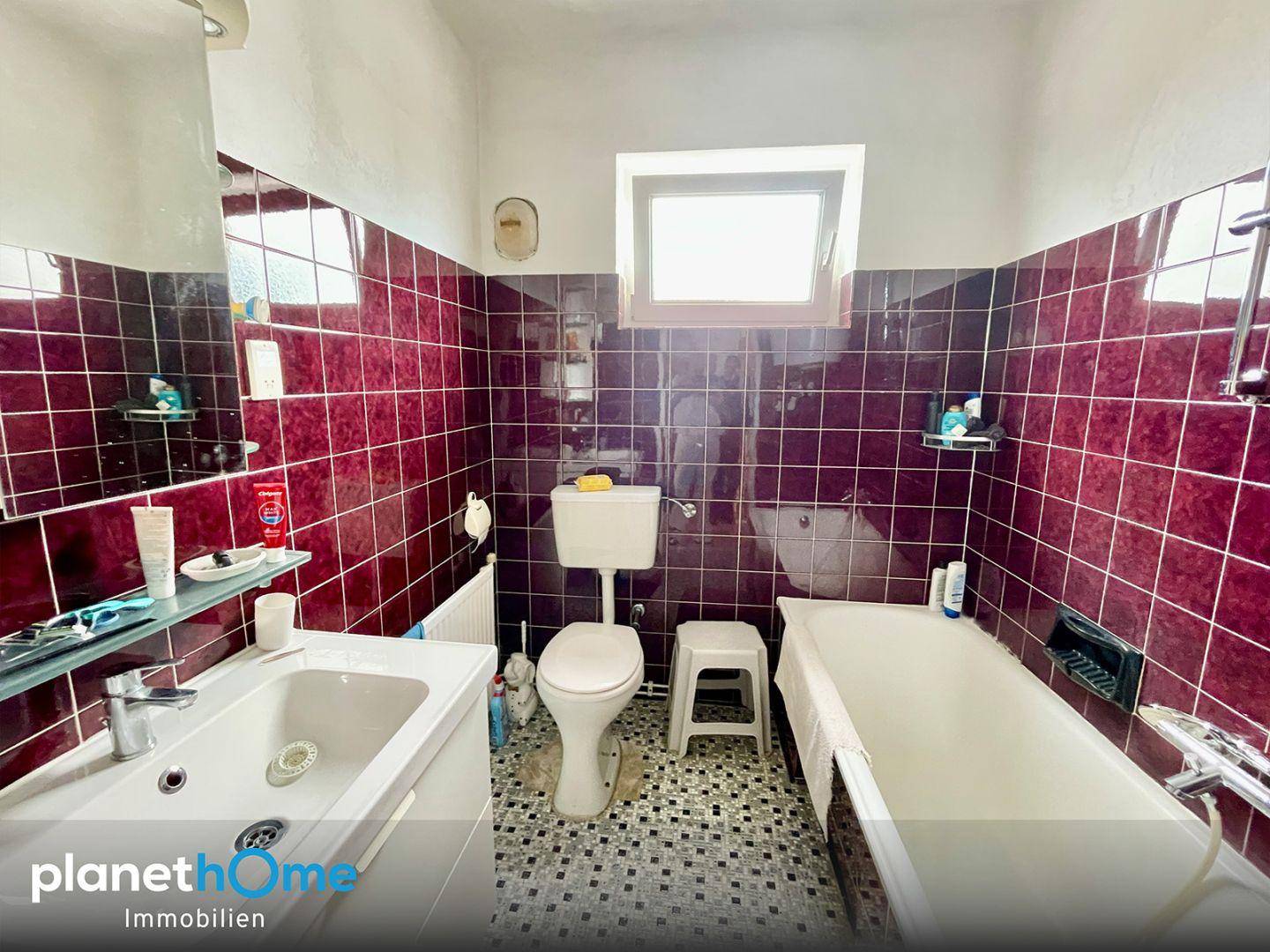 Badezimmer mit roten Fliesen, Badewanne, WC und Fenster für Tageslicht.