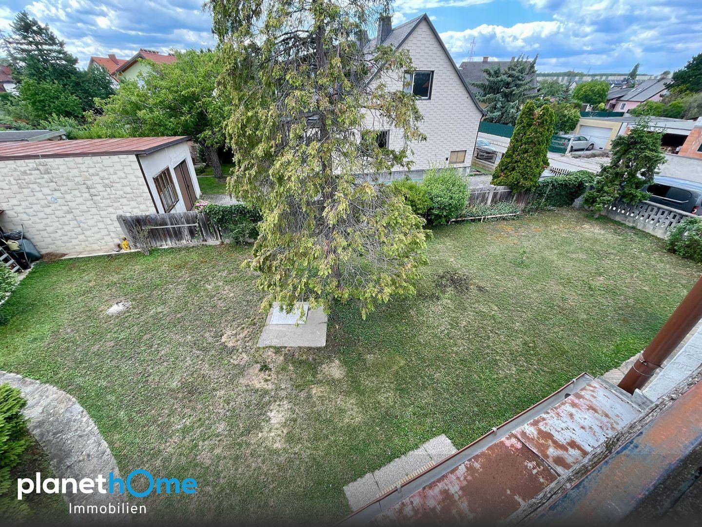 Blick von oben auf den weitläufigen Gartenbereich mit Rasenfläche und Baumbestand hinter dem Haus.