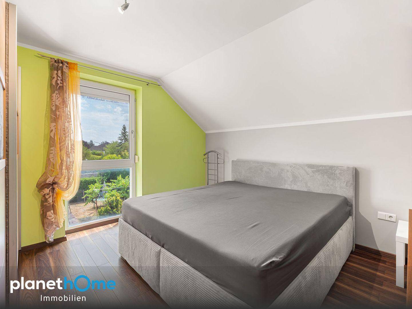 Modernes Schlafzimmer mit farbiger Wand, Holzboden und großem Fenster.