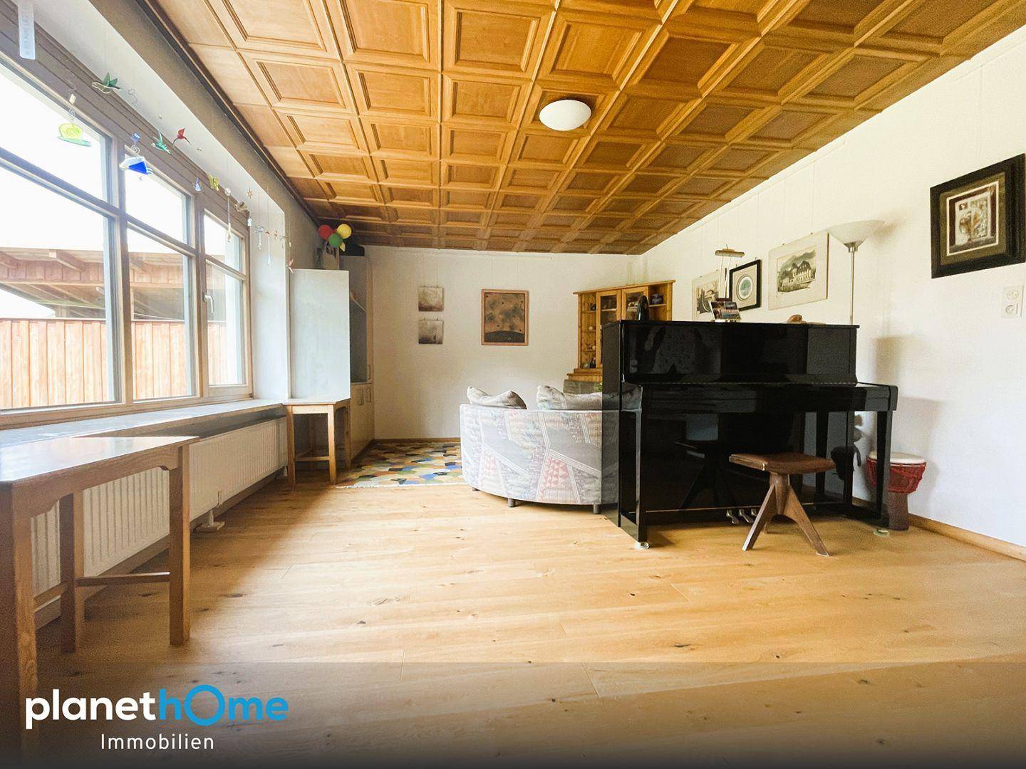 Geräumiges Wohnzimmer mit Holzkassettendecke, Parkettboden und großen Fenstern für viel Licht.