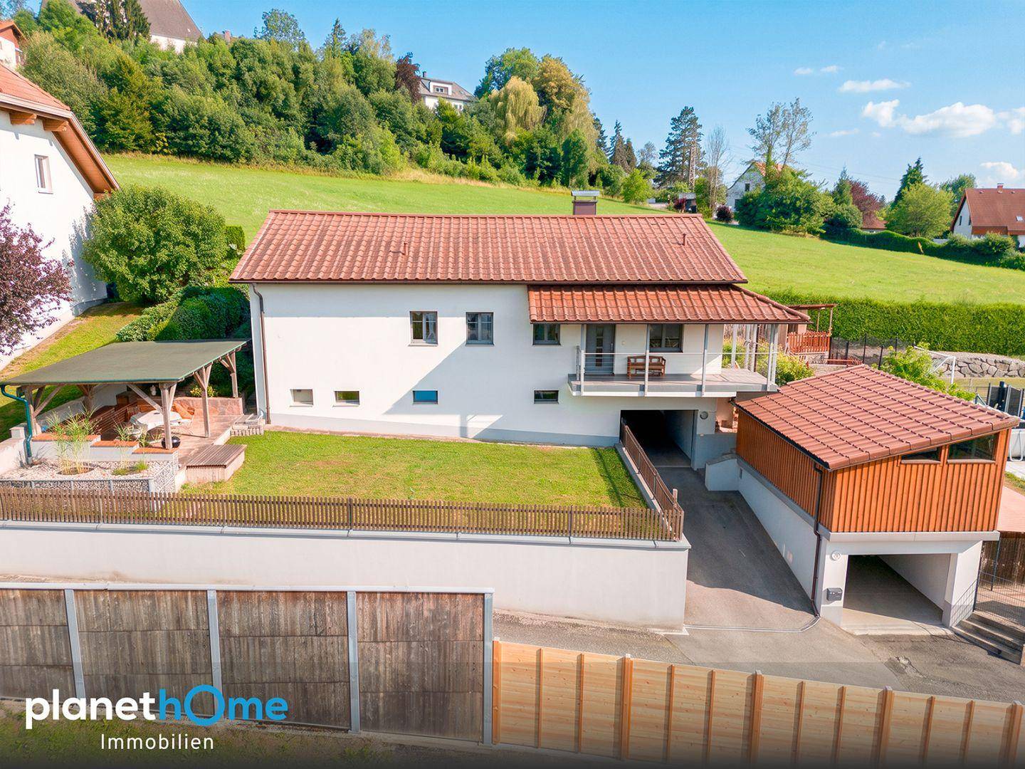 Ansicht des Hauses von der Straße mit gepflegtem Vorgarten, Garage und umliegender Natur.