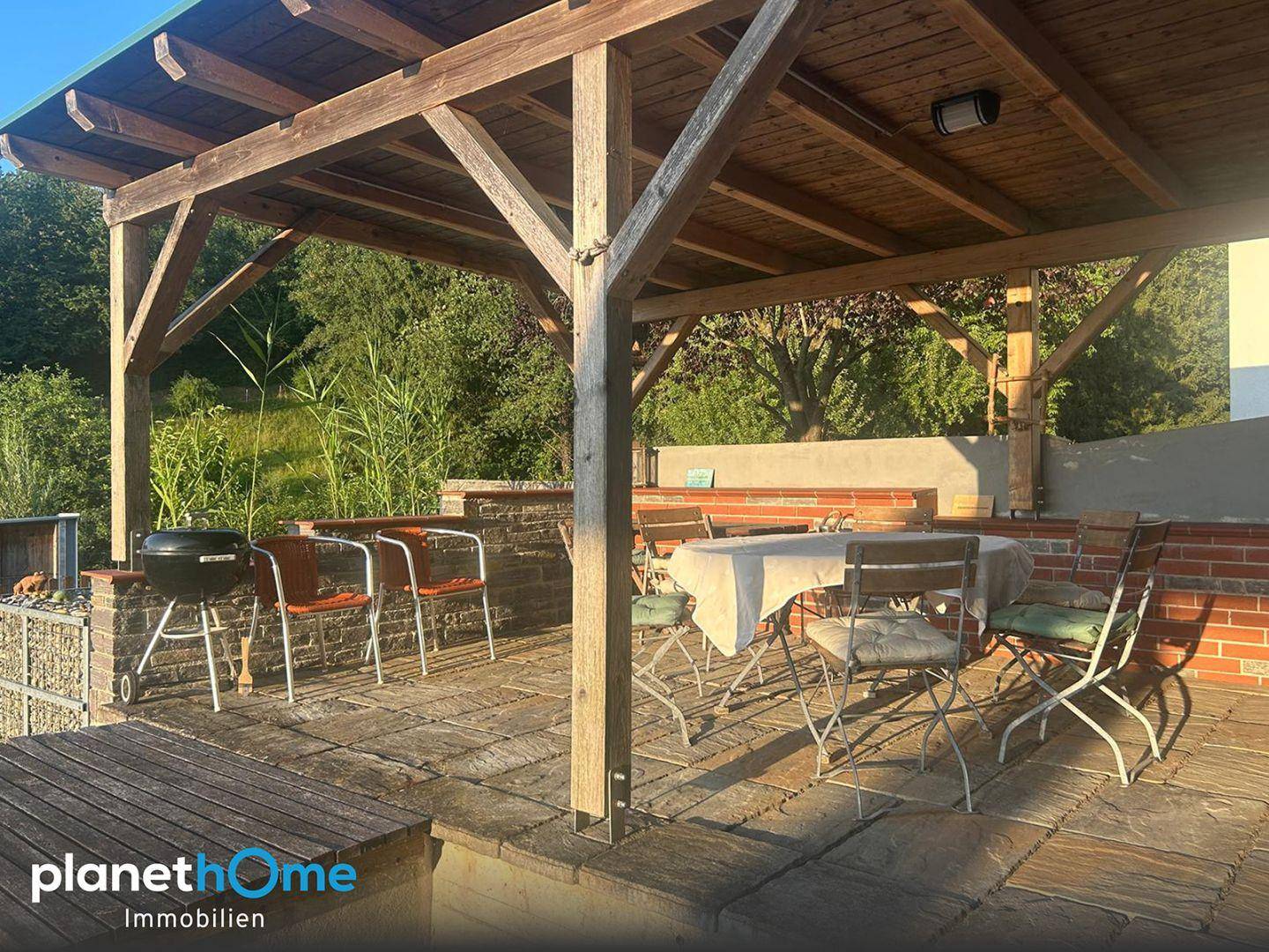 Großzügige Terrasse mit Grillbereich, Esstisch und einer schattenspendenden Holzpergola.