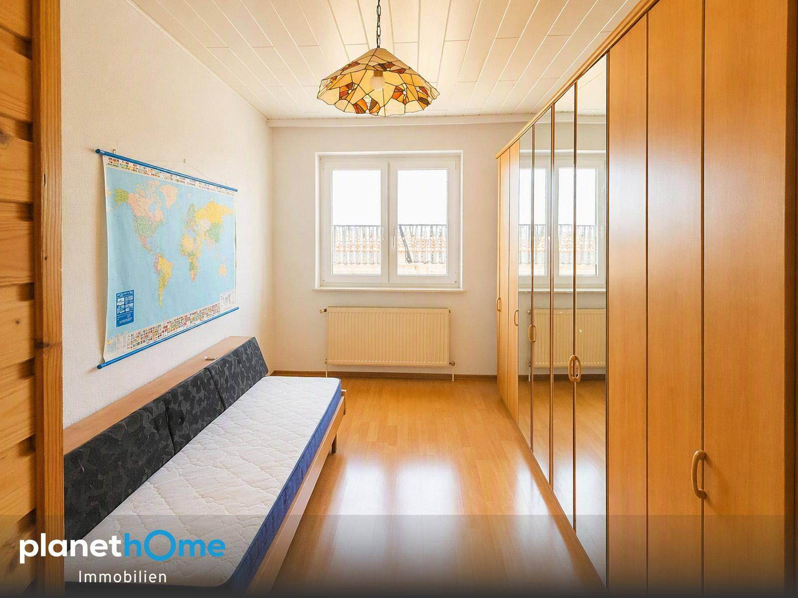 Helles Schlafzimmer mit Holzboden, Spiegelschrank und einem Fenster mit Blick nach draußen.