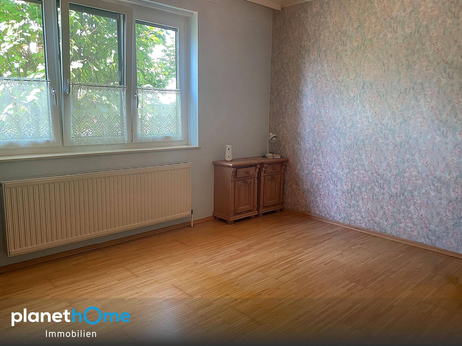 Gemütliches Zimmer mit Holzboden, gemusterter Tapete und großem Fenster.