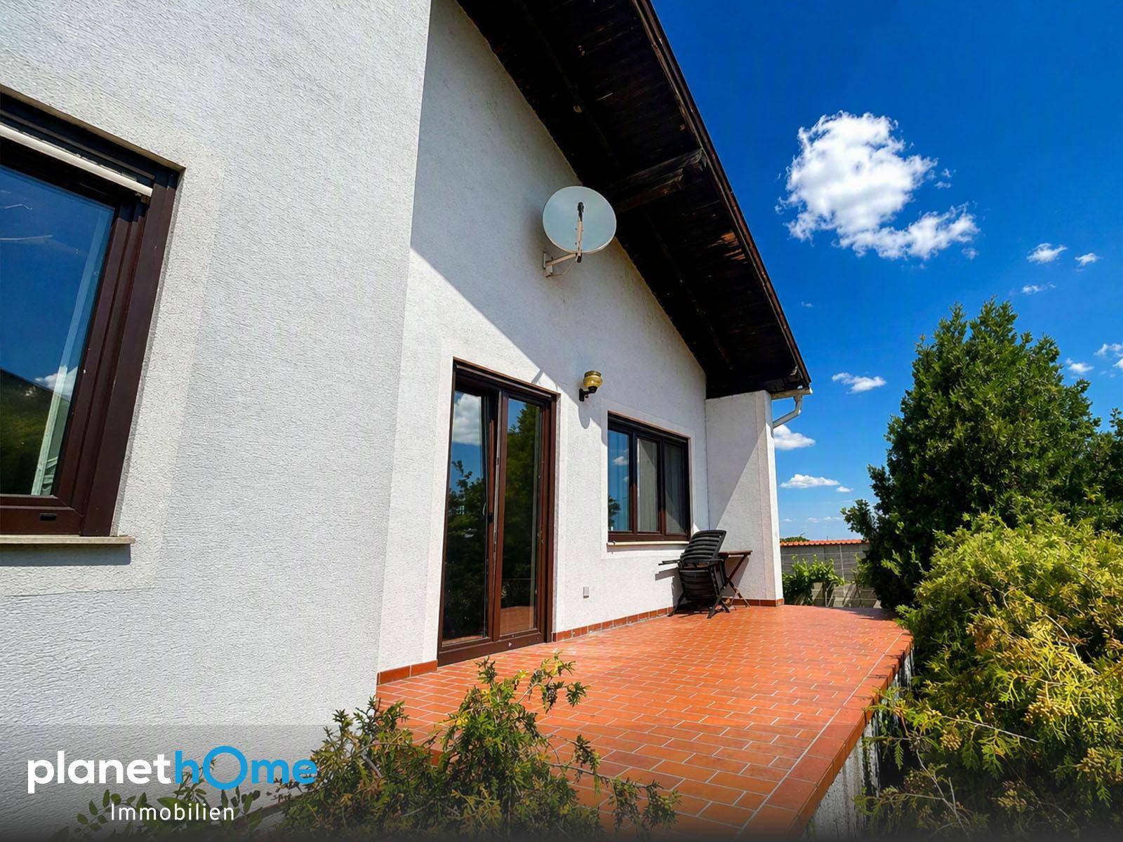 Gedeckte Terrasse mit braunen Fliesen und einem Satellitenspiegel an der Hauswand.