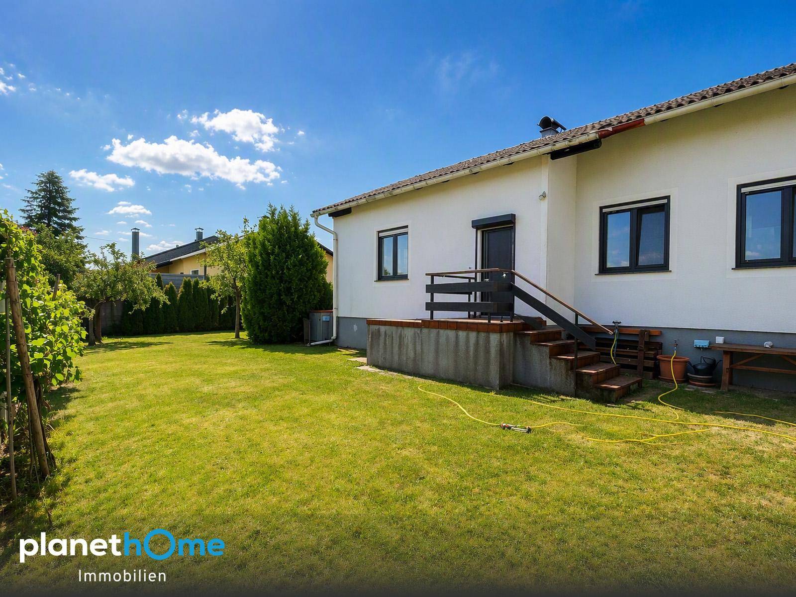 Rückseite des Hauses mit gepflegtem Rasen, kleiner Terrasse und Zugang zum Garten.