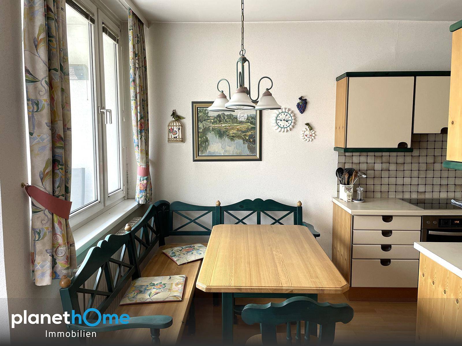 Essbereich in der Küche mit einer grünen Eckbank und einem Holztisch neben einem großen Fenster.