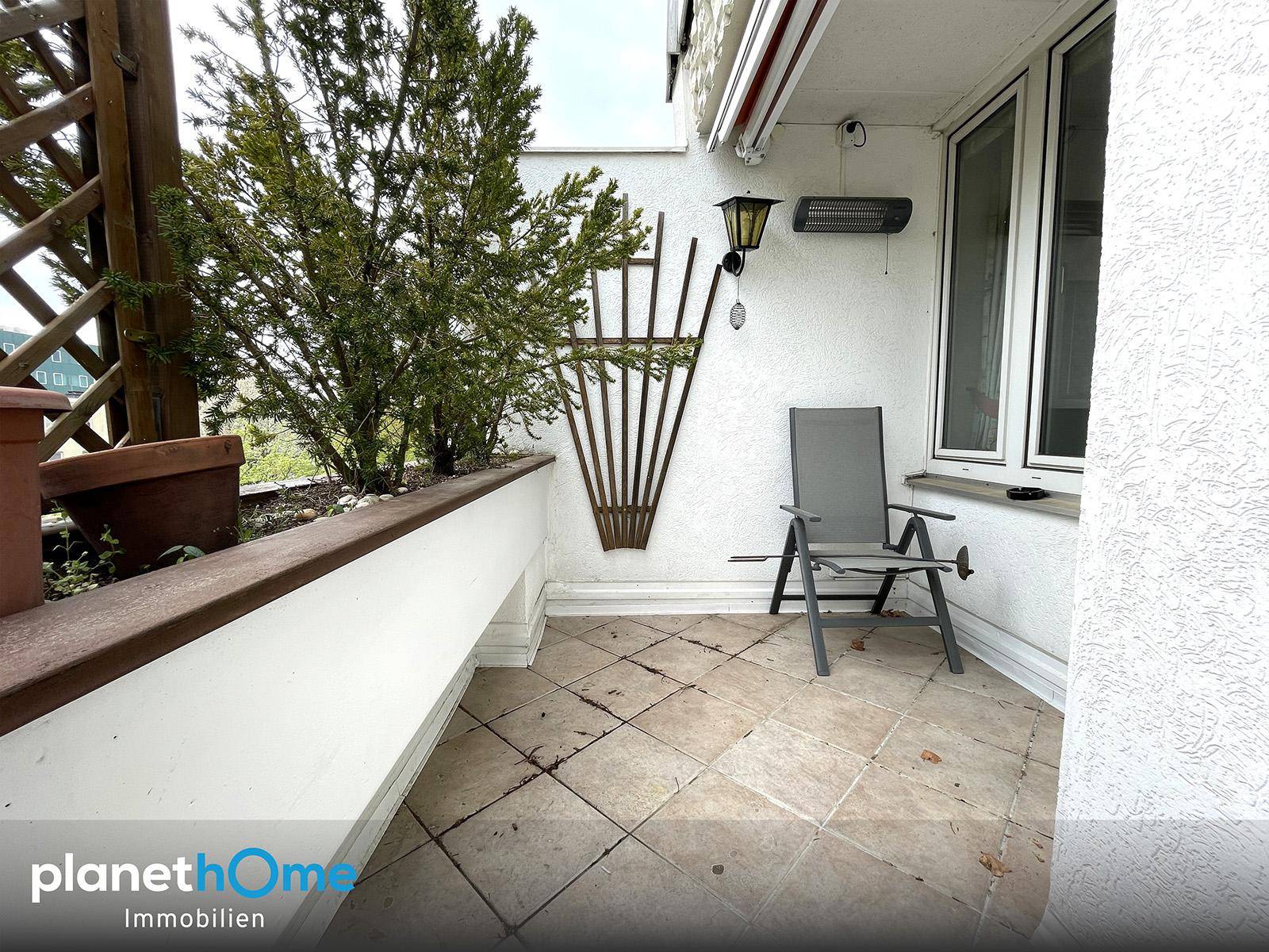Geflieste Terrasse mit Pflanzenbeet, einem Stuhl und einem Wandheizstrahler für kühle Abende.