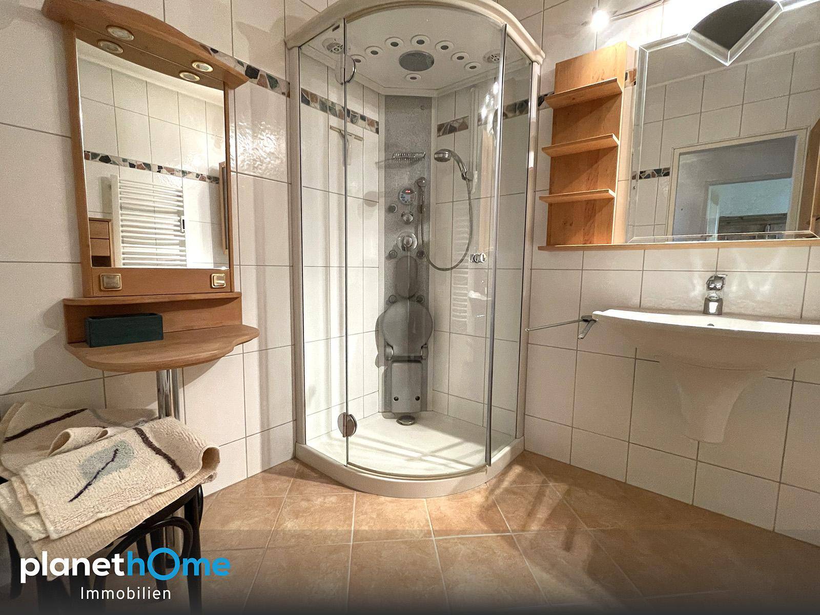 Badezimmer mit einer Eckduschkabine, einem Waschbecken und hellen Fliesen an Wänden und Boden.