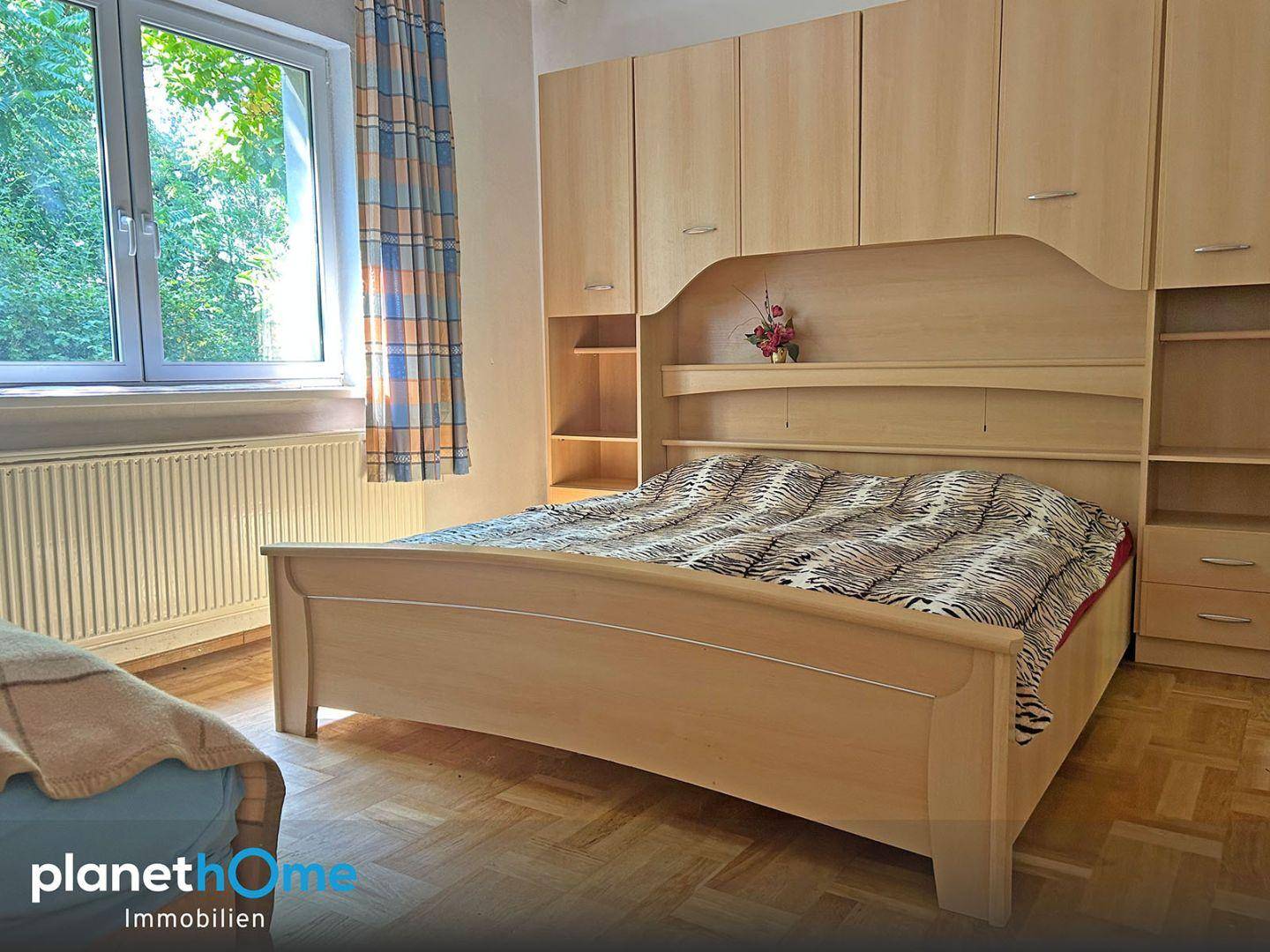 Schlafzimmer mit hellem Holzschrank, Doppelbett und Parkettboden.