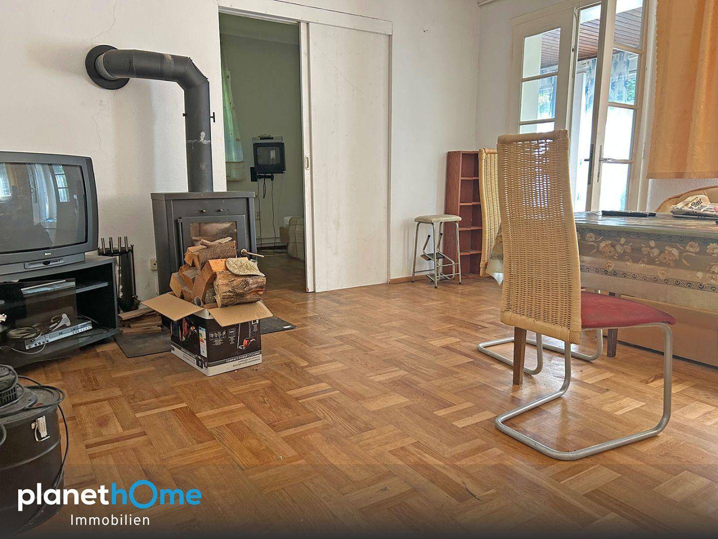 Gemütliches Wohnzimmer mit Holzofen, Fischgrätparkett und älterer Einrichtung.