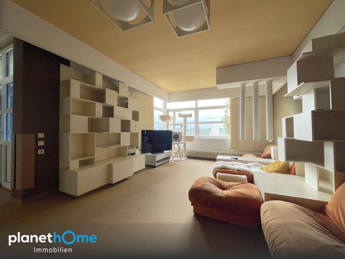 Helles Wohnzimmer mit modularen Regalen, Fernseher und Blick ins Grüne.