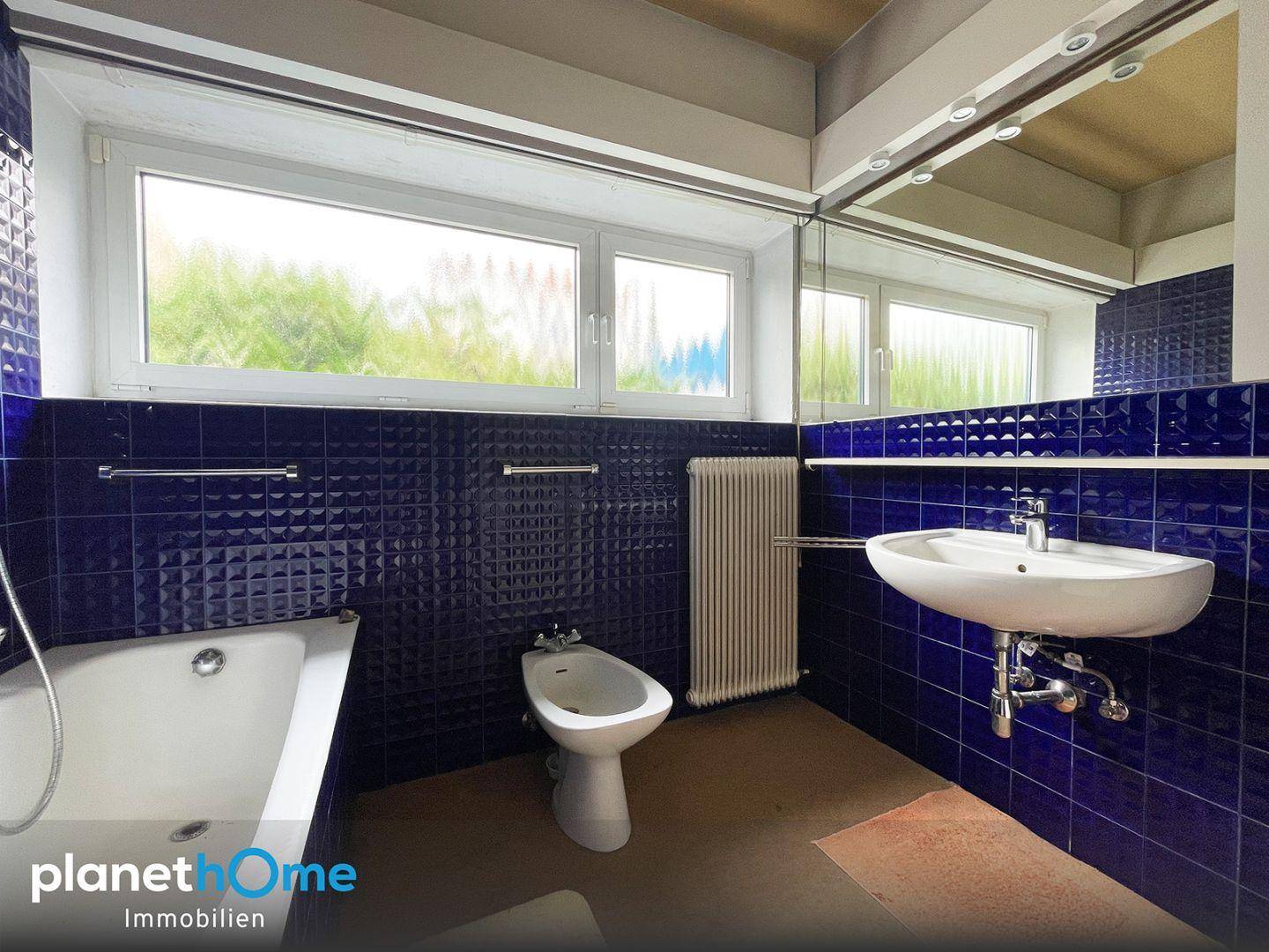 Badezimmer mit blauen Fliesen, Badewanne, Bidet und großem Fenster.