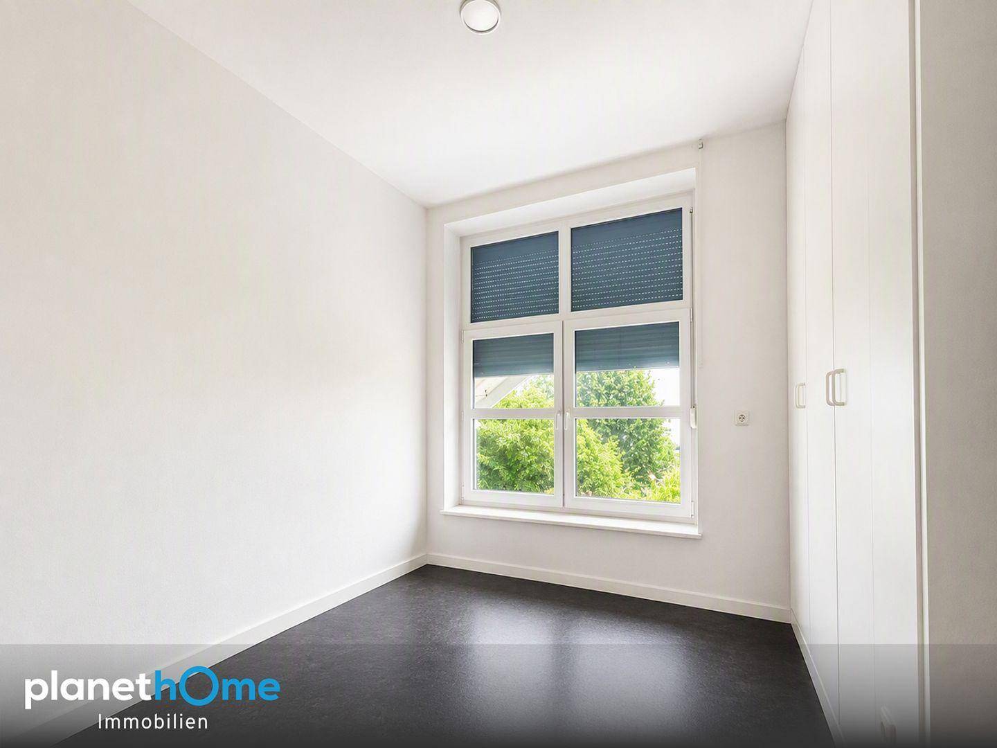 Leerer Raum mit weißen Wänden, dunklem Boden und Fenster mit Rollläden.