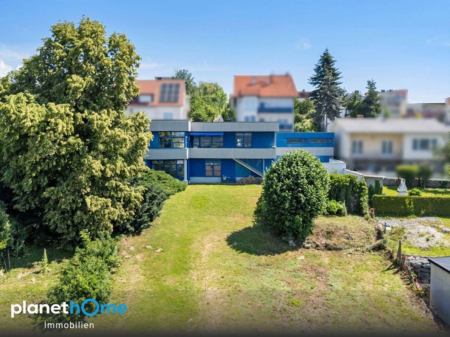 Weitläufiger Gartenbereich mit Rasenfläche und dem blauen Gebäude im Hintergrund.