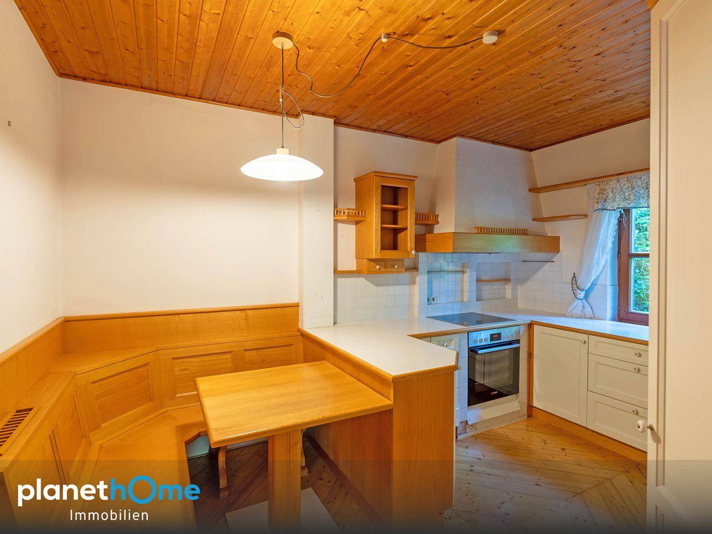 Gemütliche Küche mit Holzbalkendecke, integrierter Sitzecke und weißen Küchenschränken mit Geräten.