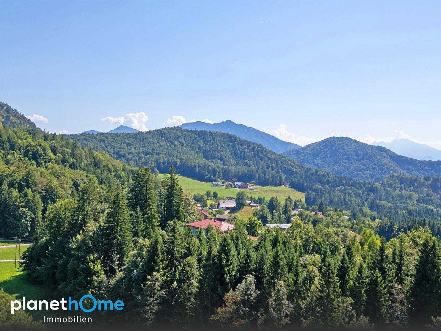 Malerischer Ausblick auf eine weite grüne Landschaft mit bewaldeten Bergen und Tälern unter blauem Himmel.